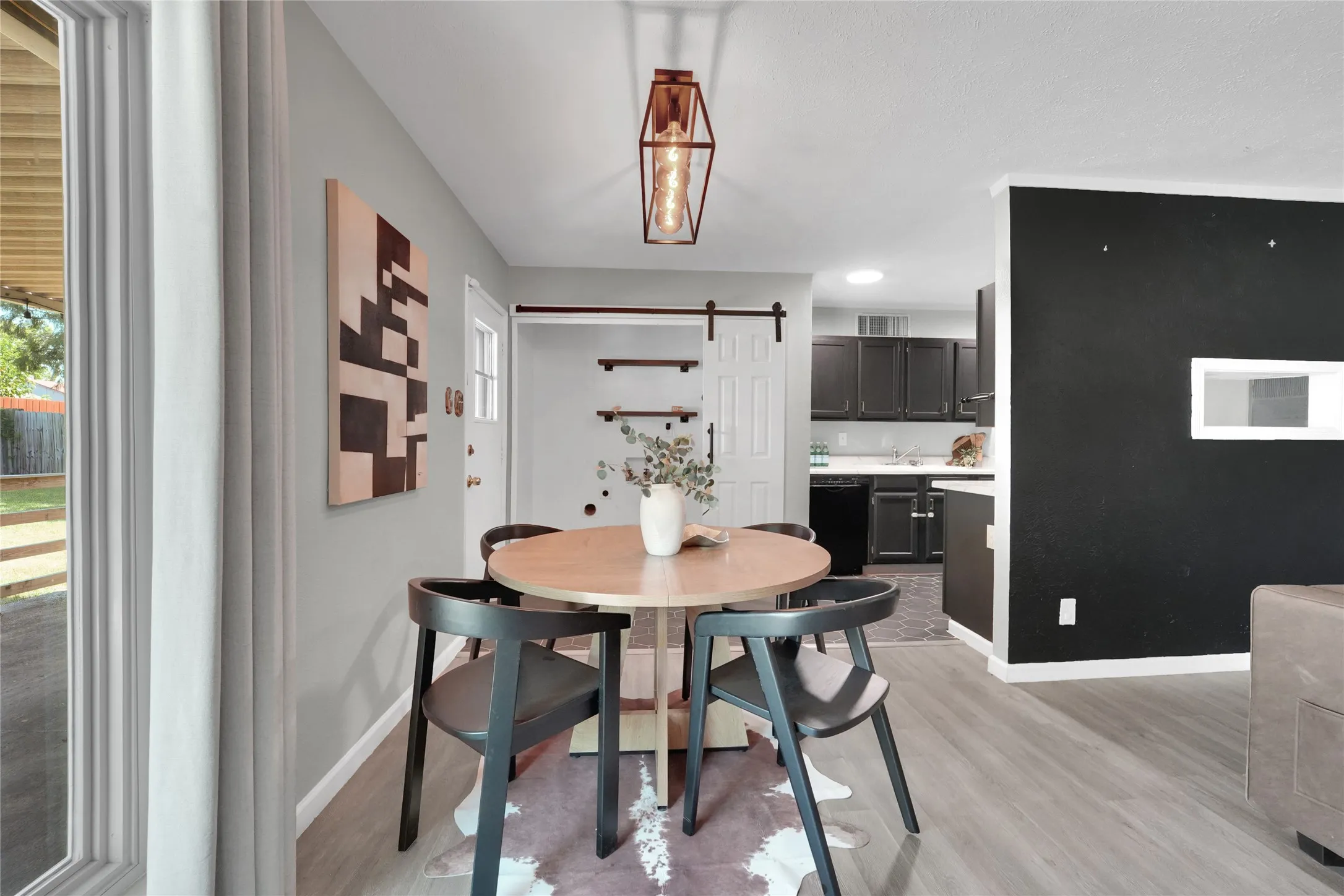 Open-concept living space featuring wood-finish flooring, a contemporary ceiling light fixture, a sliding barn door, and a kitchen with dark cabinetry