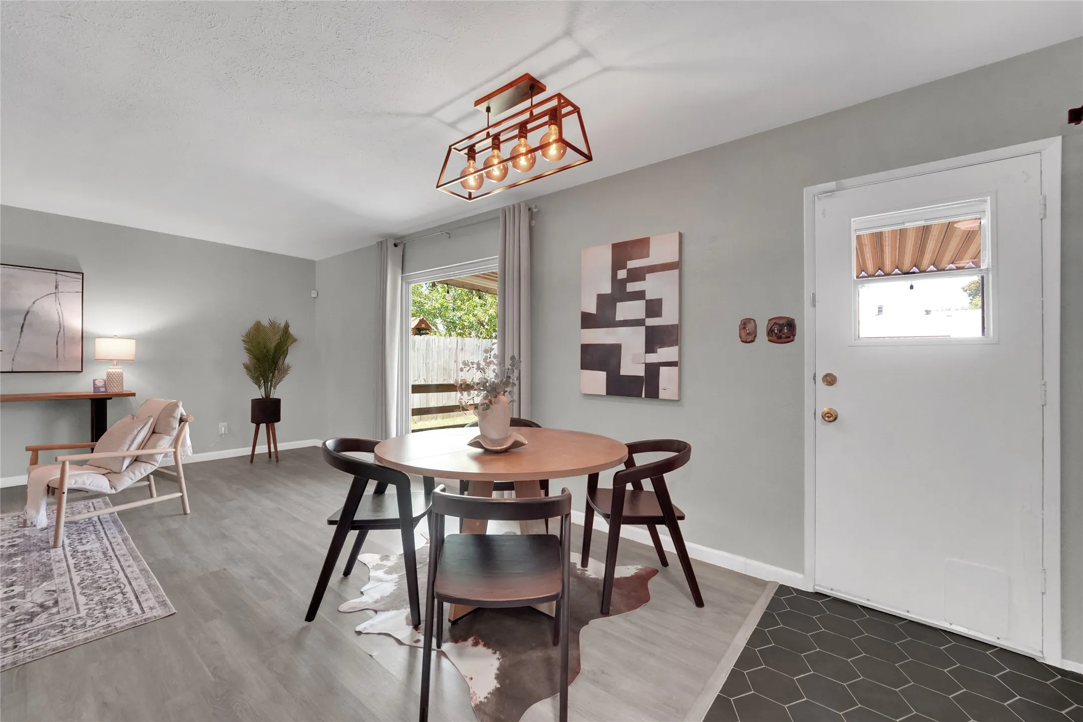 Open-concept living space with light gray walls, wood-finish flooring, and a modern rectangular chandelier