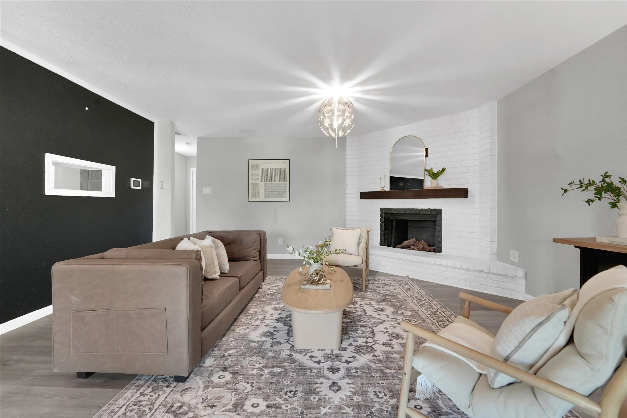 Living area featuring a white-painted brick fireplace with a dark wood mantel, a modern chandelier, and wood-finish flooring