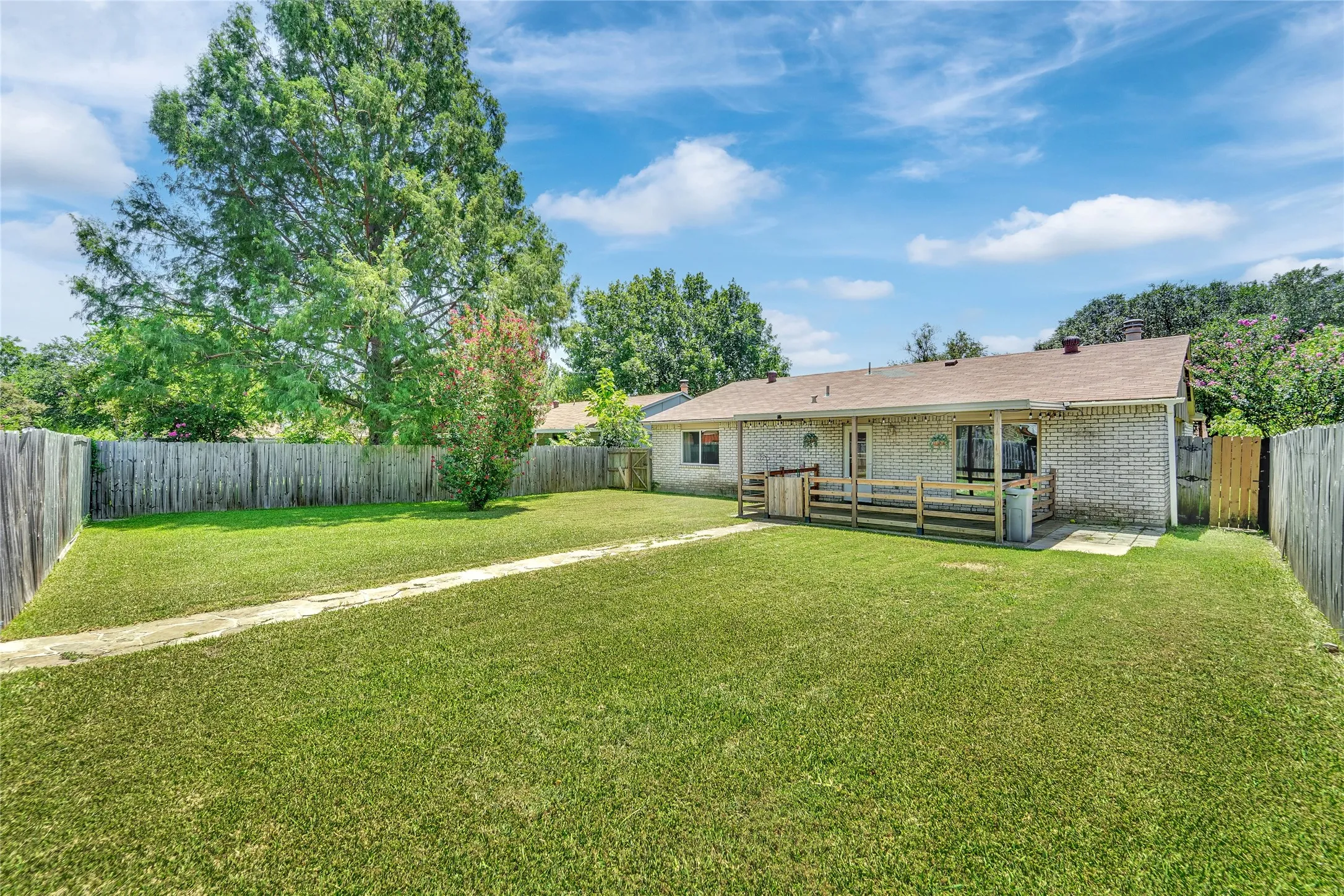 Expansive backyard featuring a lush lawn, privacy fencing, and a covered patio area with a wood railing