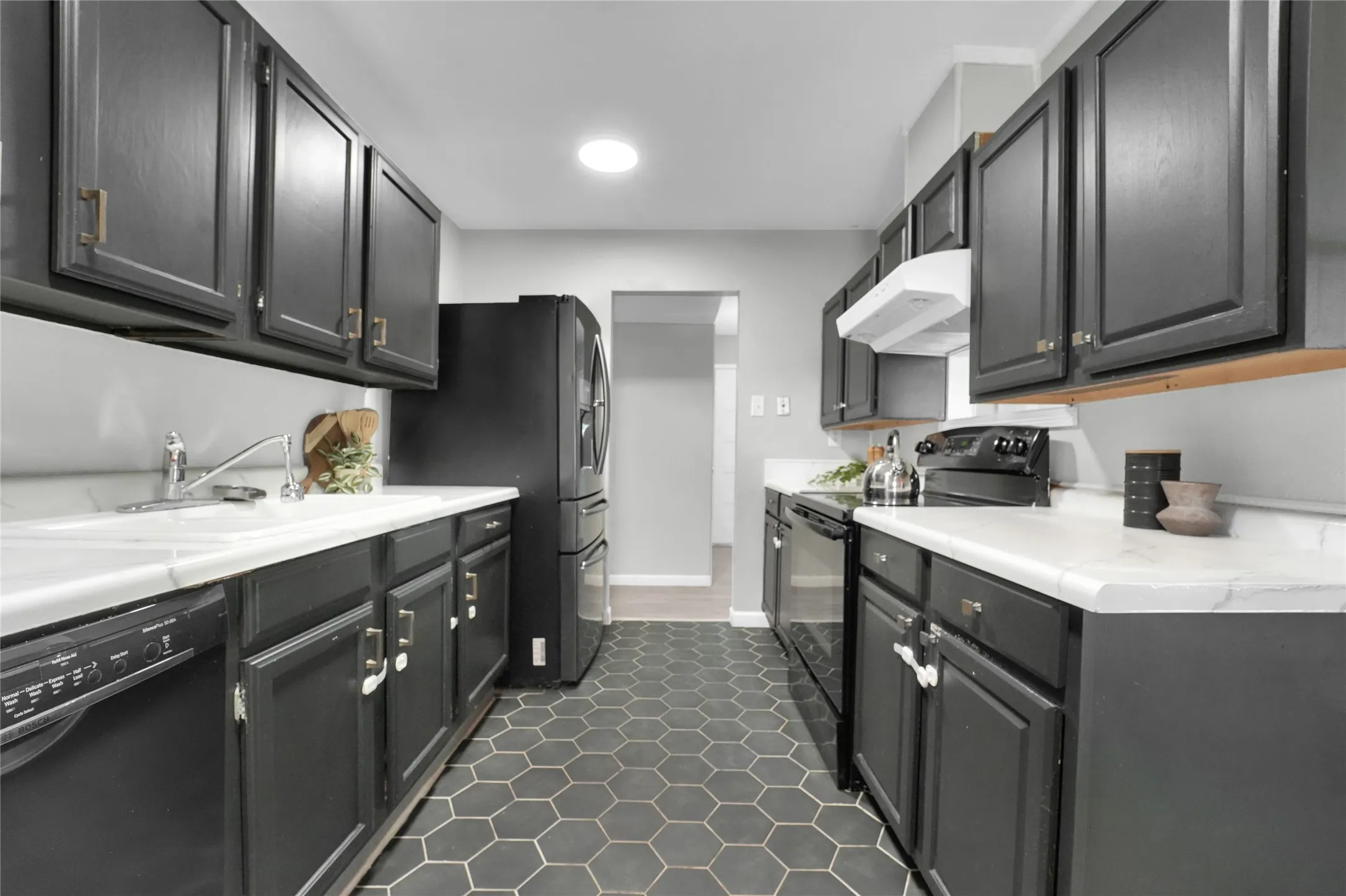 Contemporary kitchen featuring dark cabinetry with gold-tone hardware, a white undermount sink, and black appliances