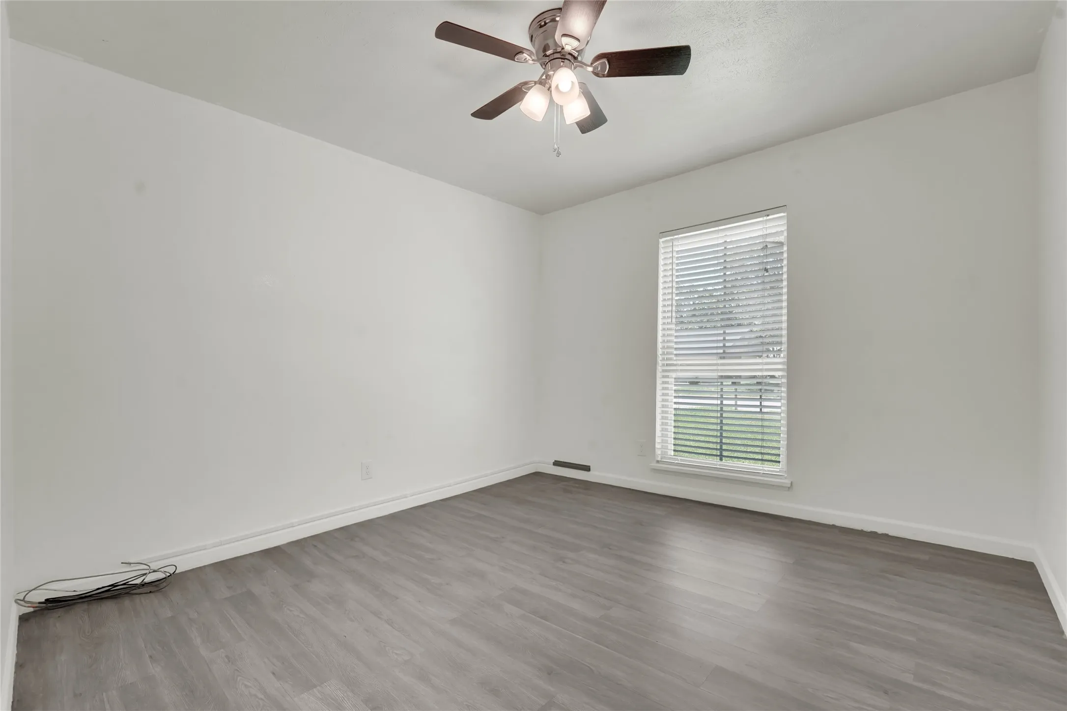 Room featuring wood-finish flooring, a window with blinds, and a ceiling fan with integrated lighting