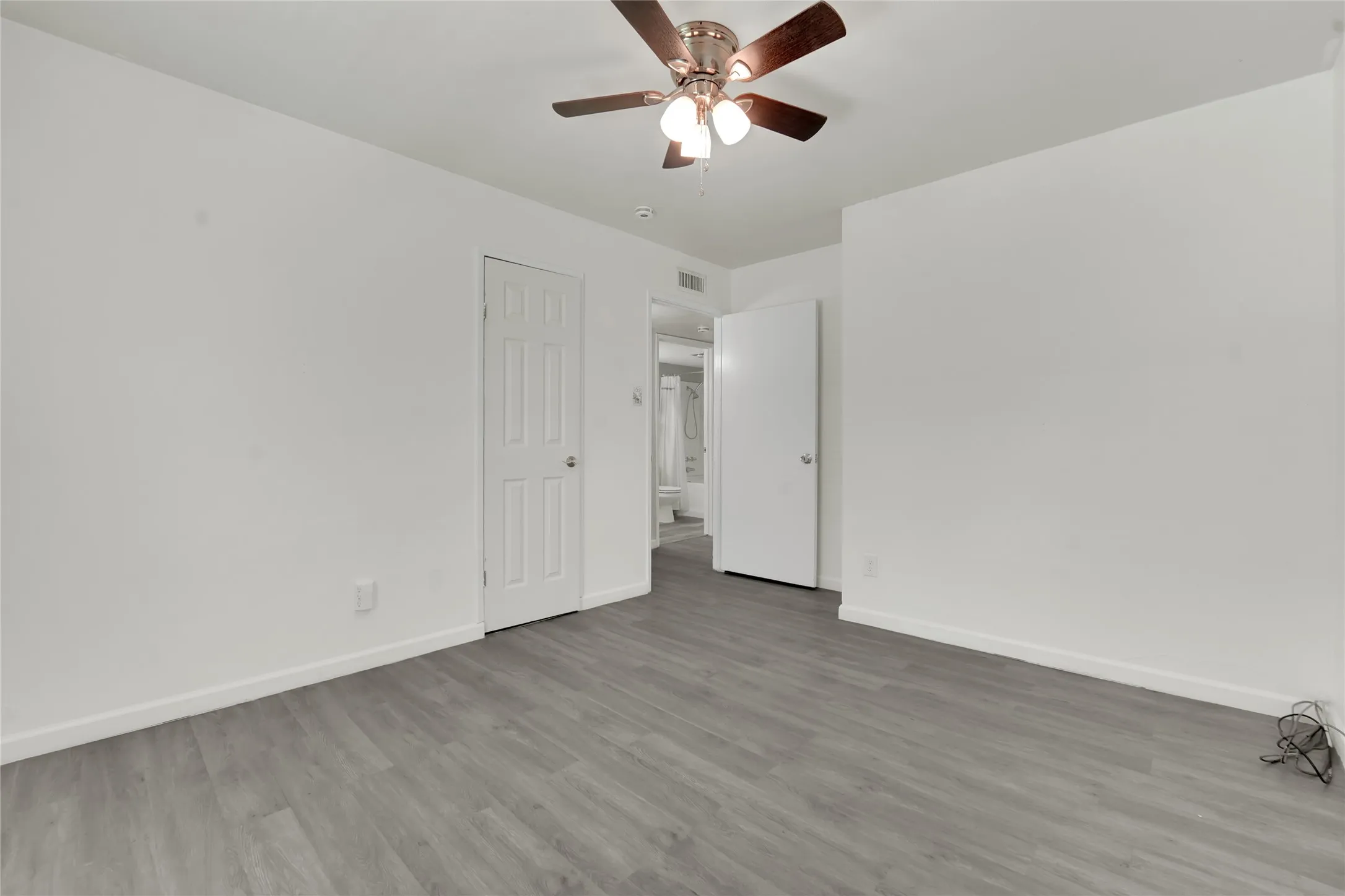 Spacious room featuring light gray wood-finish flooring, white walls, and a ceiling fan with integrated lighting
