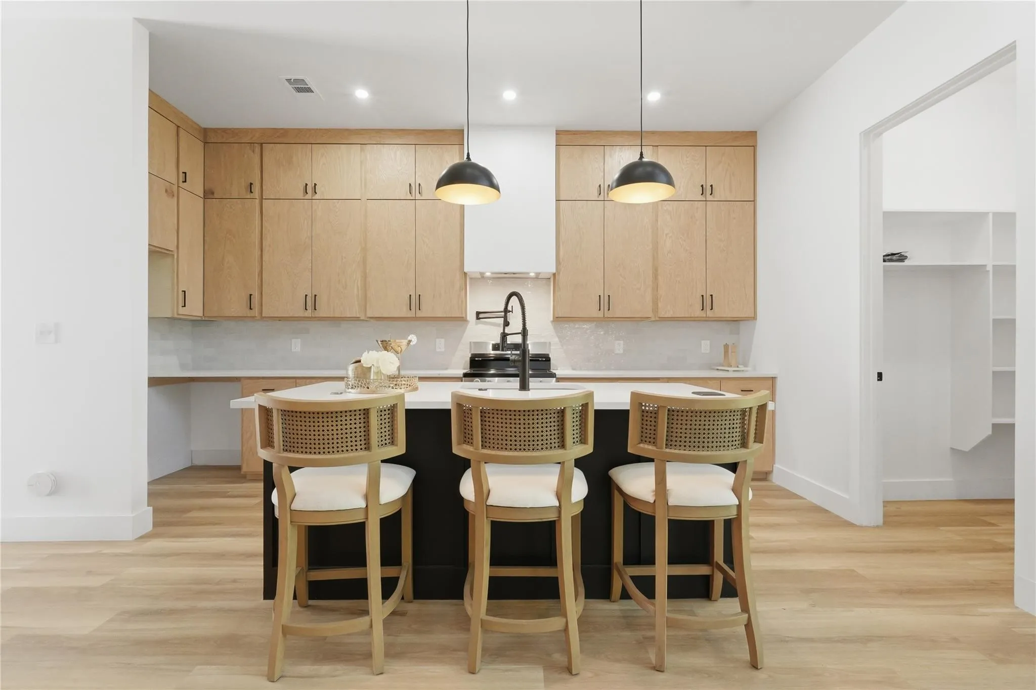 Modern kitchen featuring a central island with seating, light wood-finish cabinetry, white countertops, and a subway tile backsplash