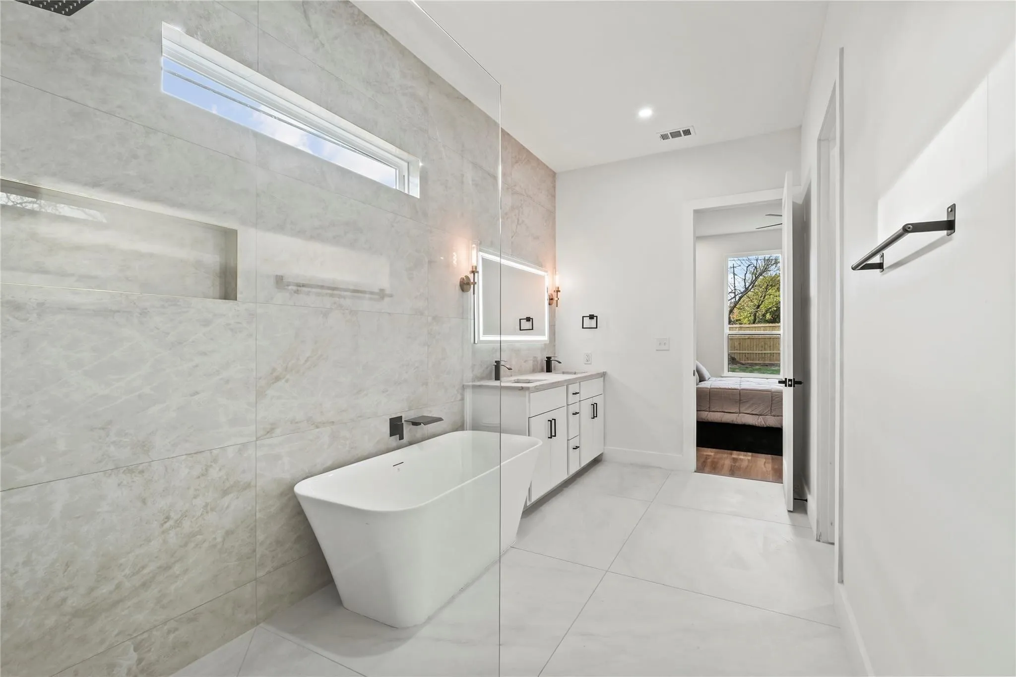 Spacious bathroom featuring a freestanding soaking tub, large format floor and wall tiles, and a transom window
