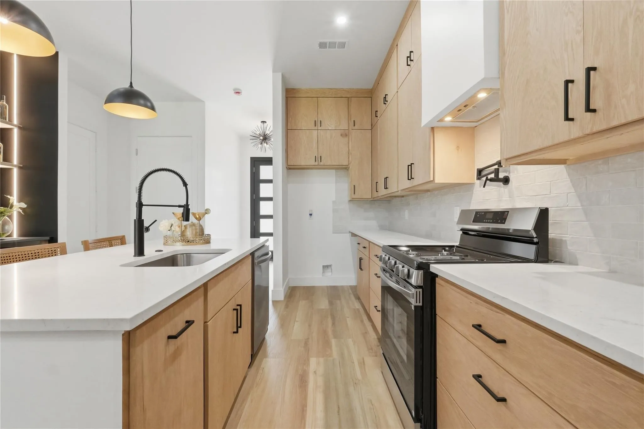 Modern kitchen featuring light wood-finish cabinetry, white countertops, and stainless steel appliances