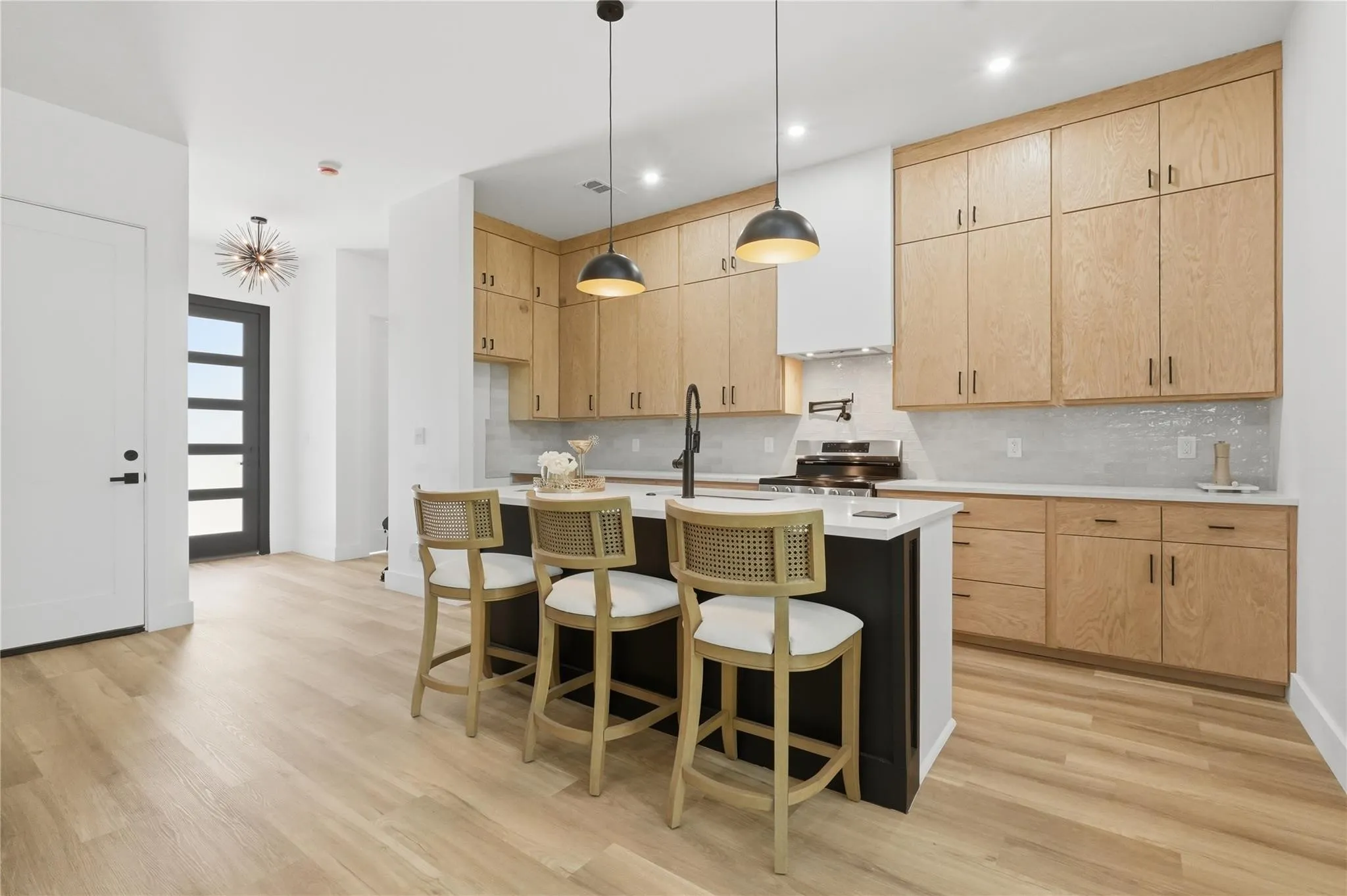 Modern kitchen featuring light wood-finish cabinetry, a central island with a dark base and light countertop, and pendant lighting