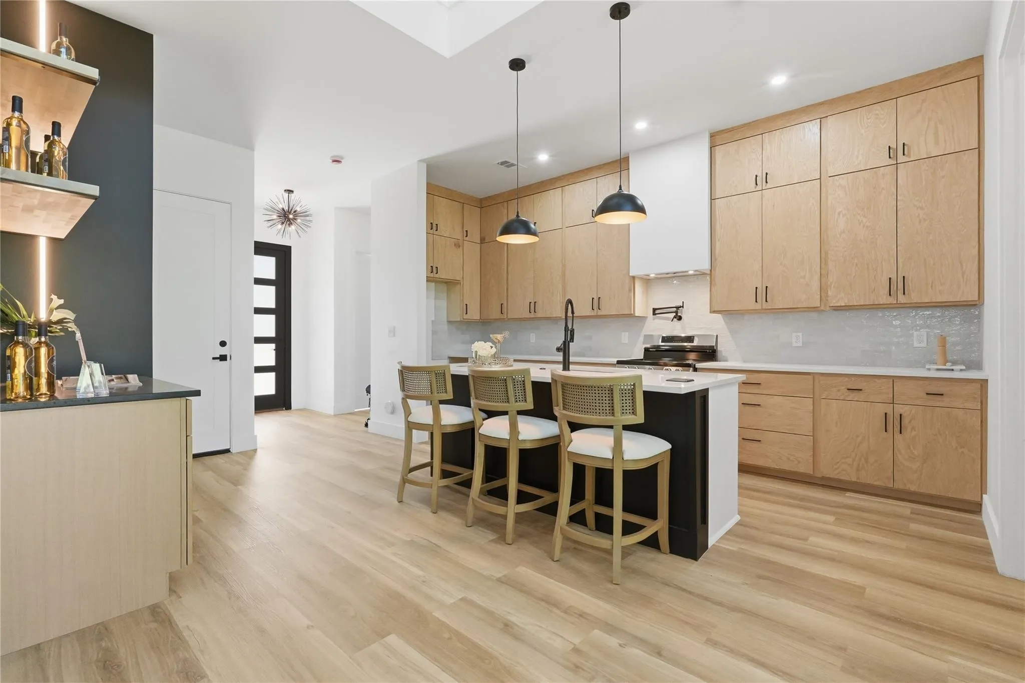 Modern kitchen featuring light wood-finish cabinetry, a central island with bar seating, and light-toned flooring