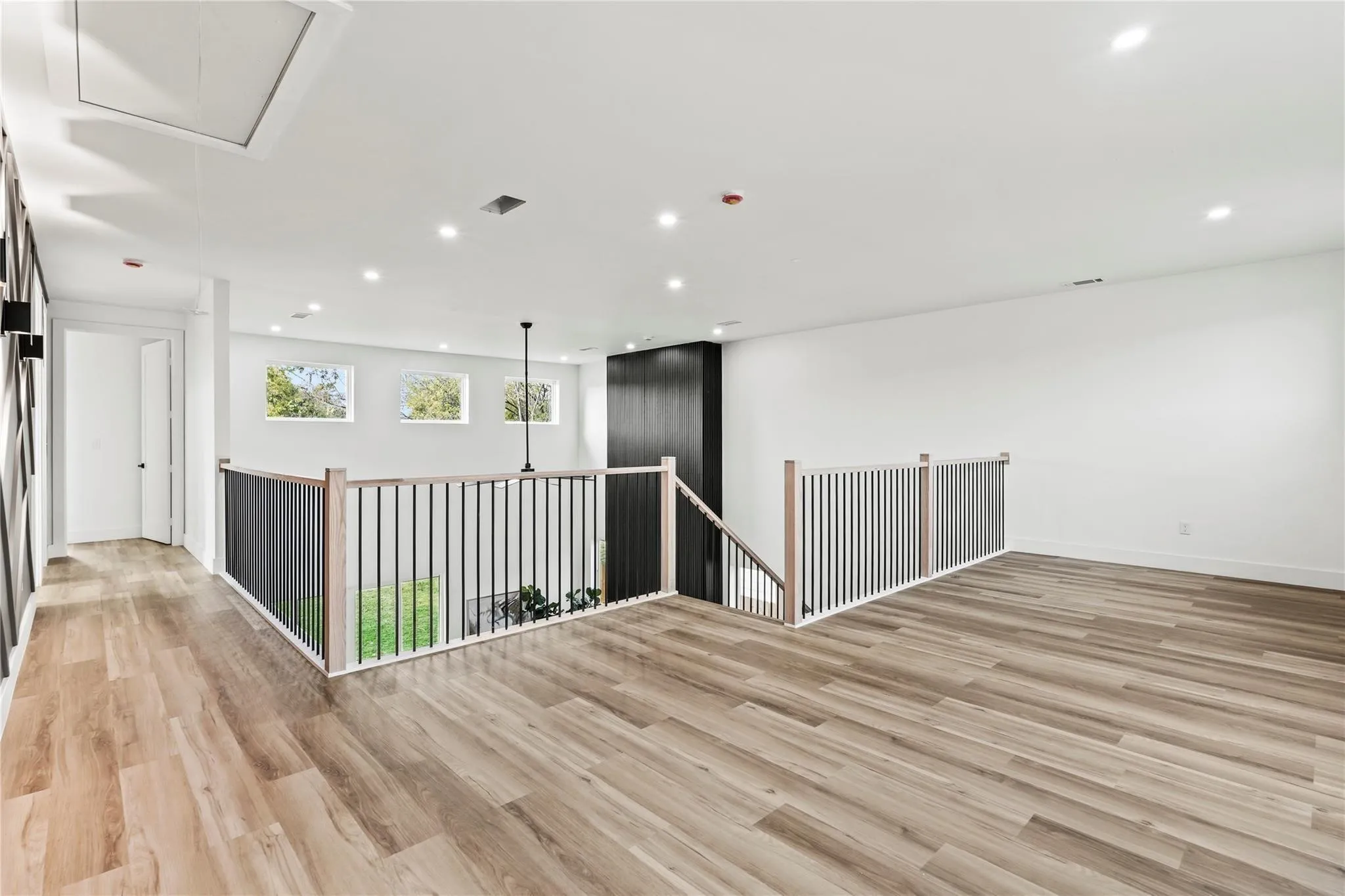 Open concept loft area featuring wood-finish flooring, recessed lighting, and a modern stair railing with wood handrails and black balusters