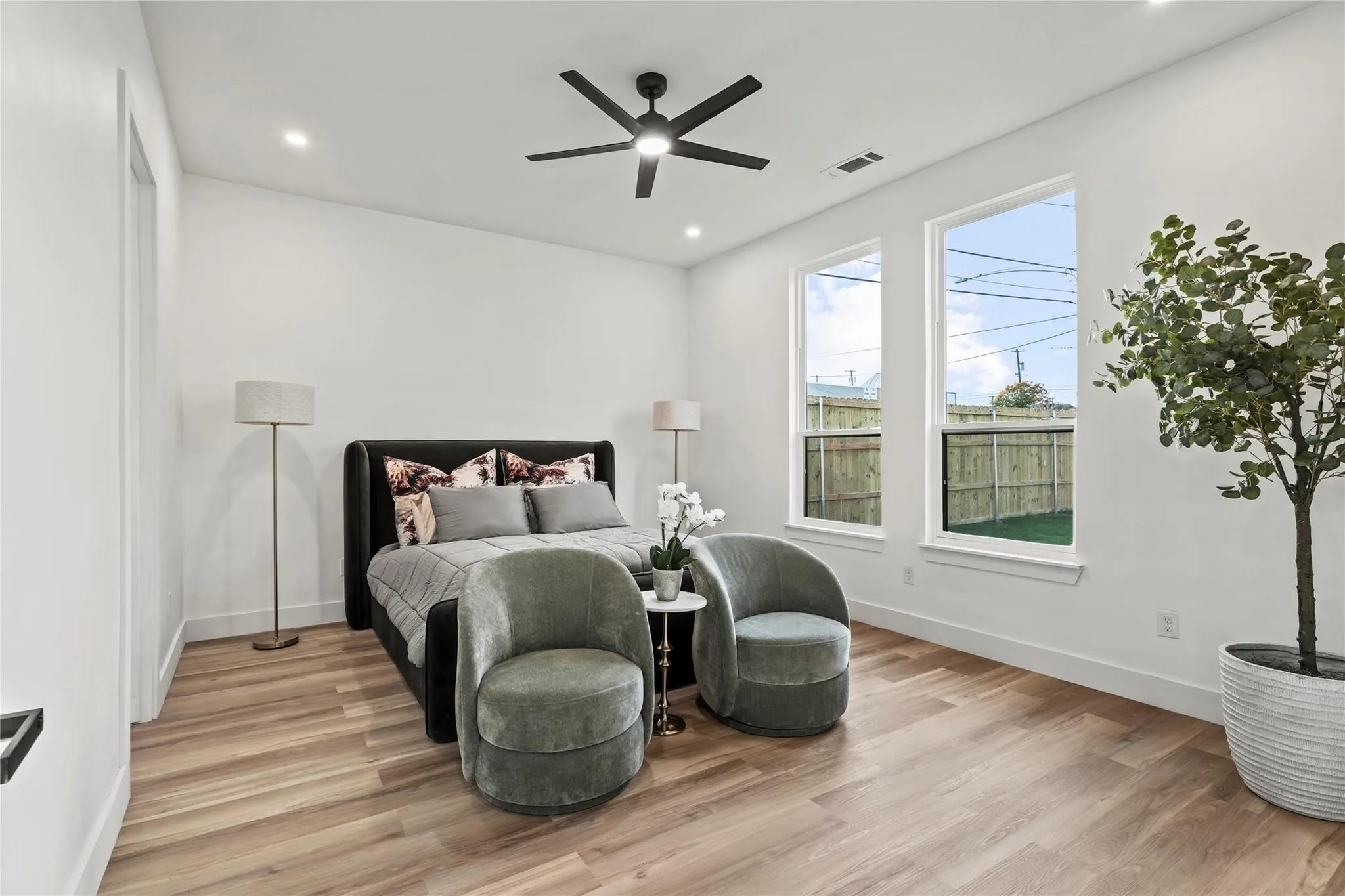 Spacious room featuring wood-finish flooring, two tall windows, and a ceiling fan with integrated lighting