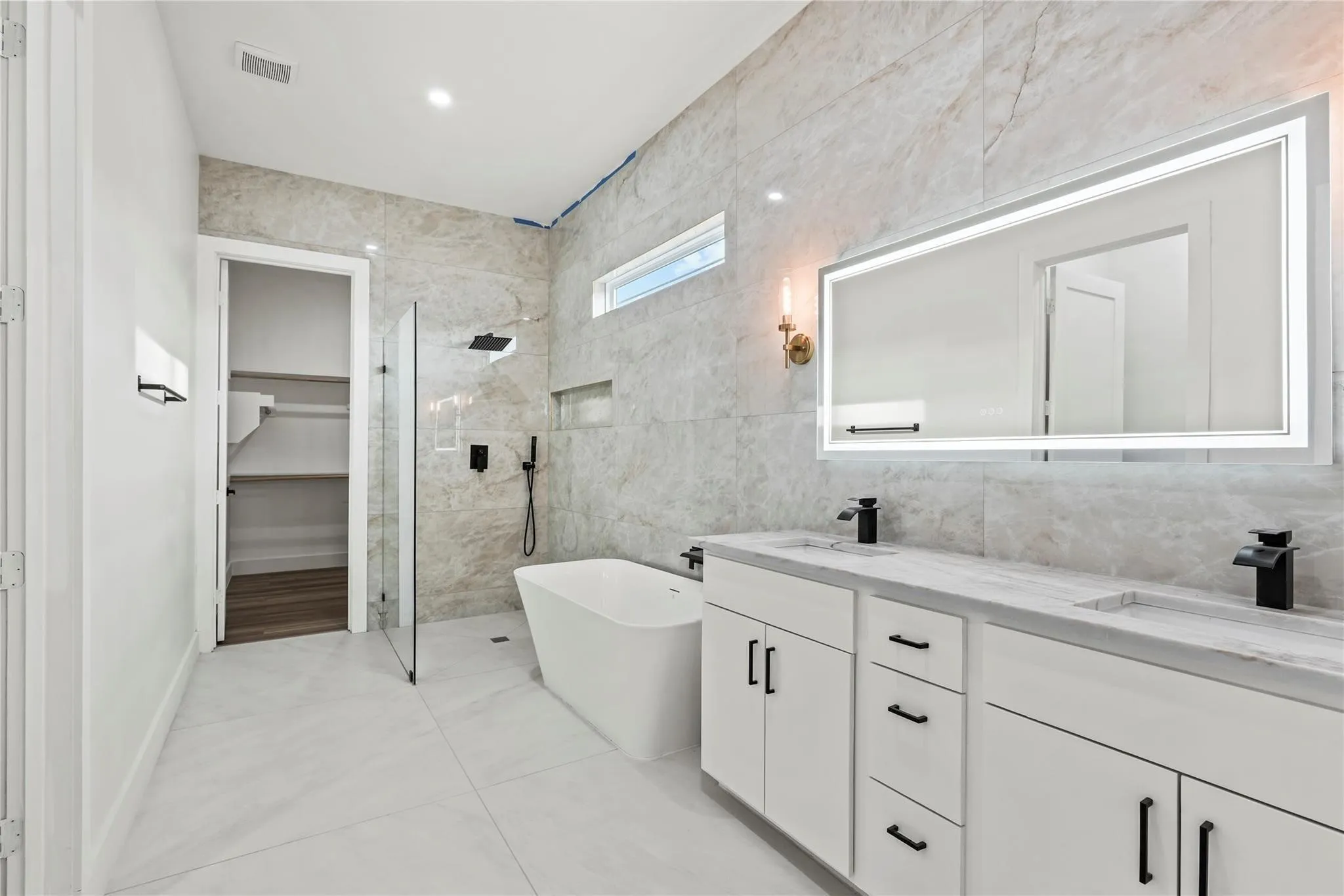 Contemporary bathroom featuring a freestanding tub, glass-enclosed shower, dual vanity with undermount sinks, and an illuminated mirror
