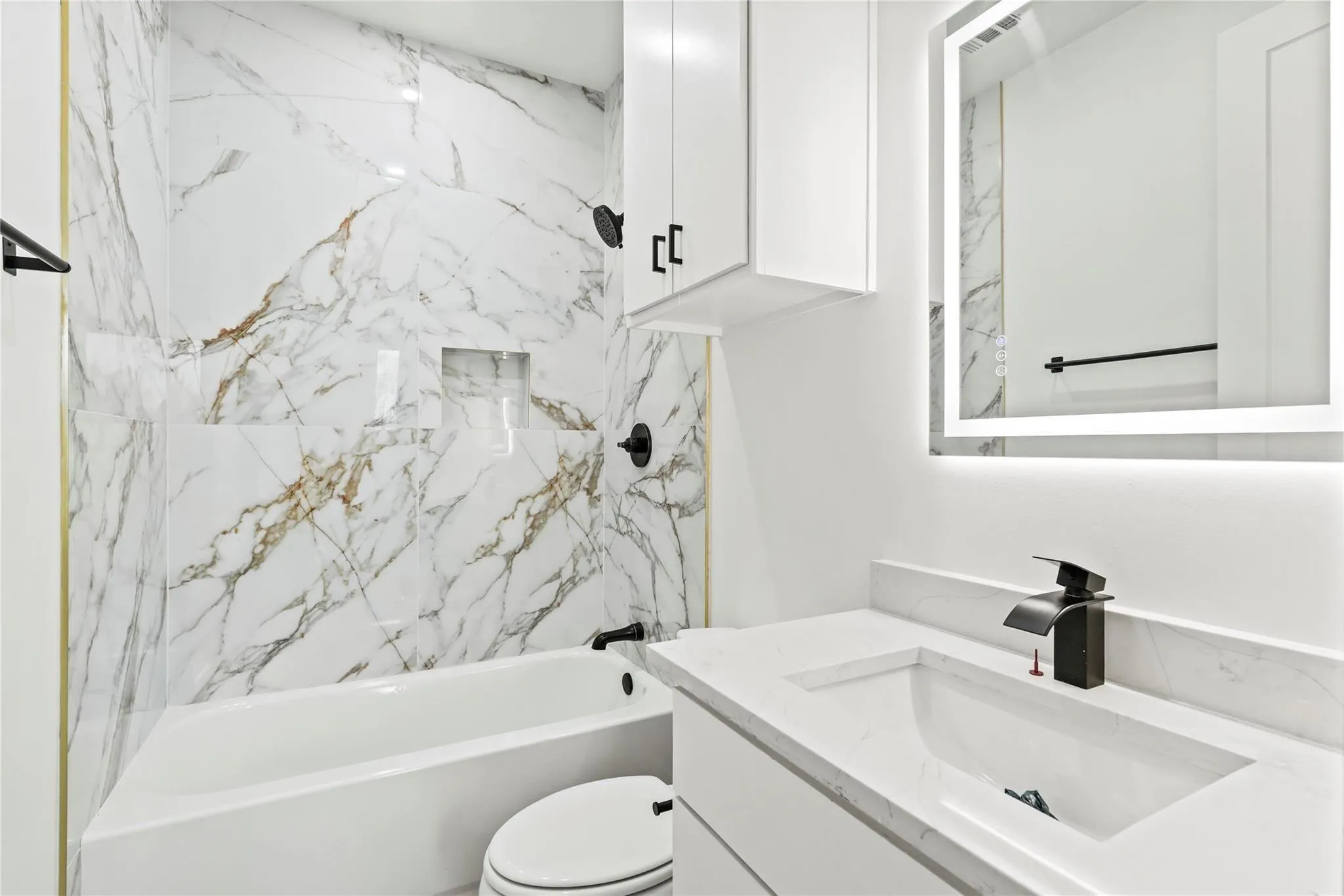 Bathroom featuring a built-in tub with a tiled surround, a wall-mounted showerhead, and an integrated niche