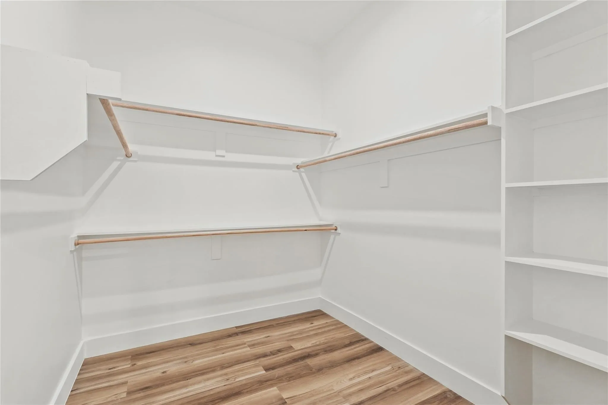 Walk-in closet featuring wood-finish flooring, white baseboards, white walls, multiple hanging rods, and built-in shelving