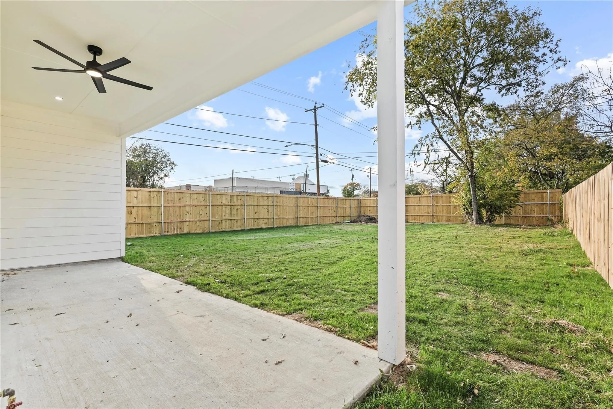 Expansive backyard featuring a covered patio with a ceiling fan, concrete slab, and a wood privacy fence