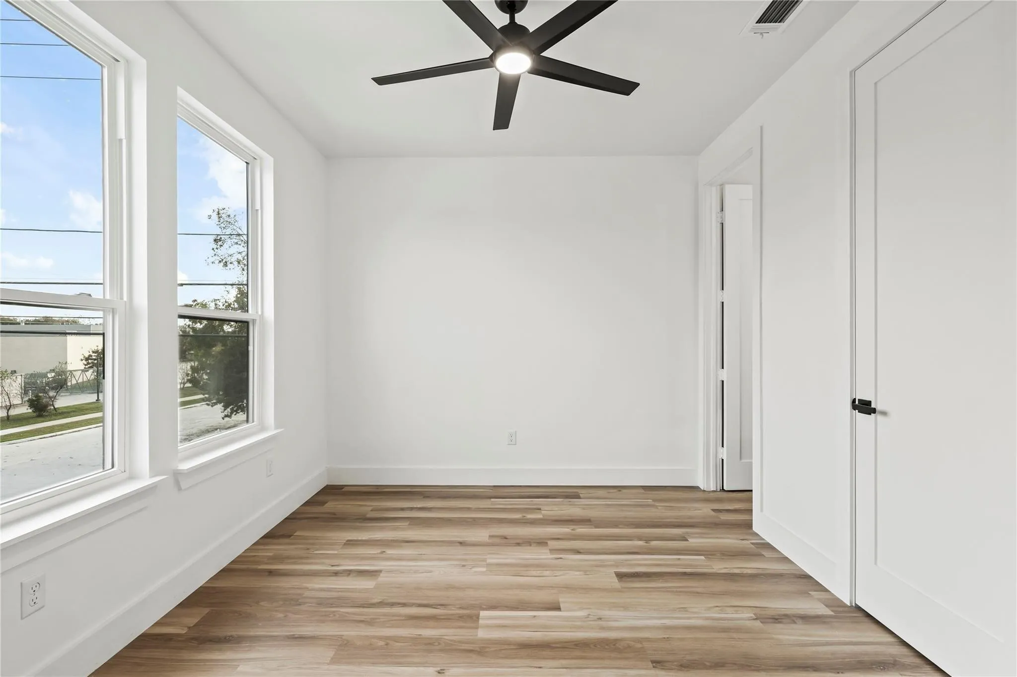Bright room featuring two windows with white trim, wood-finish flooring, a modern black ceiling fan, and crisp white walls