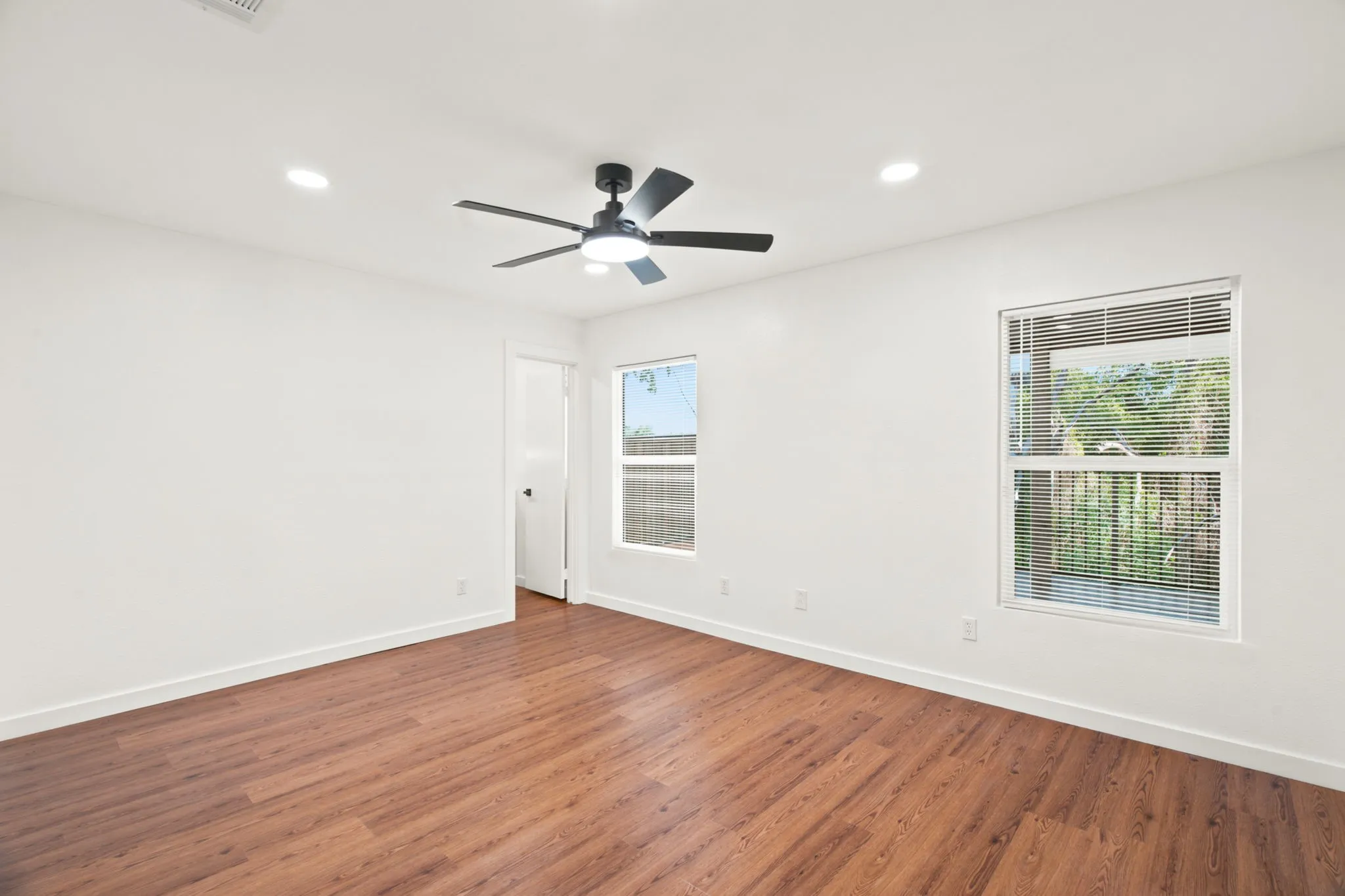 Room featuring wood-finish flooring, two windows with blinds, a ceiling fan with integrated lighting, and recessed ceiling lights