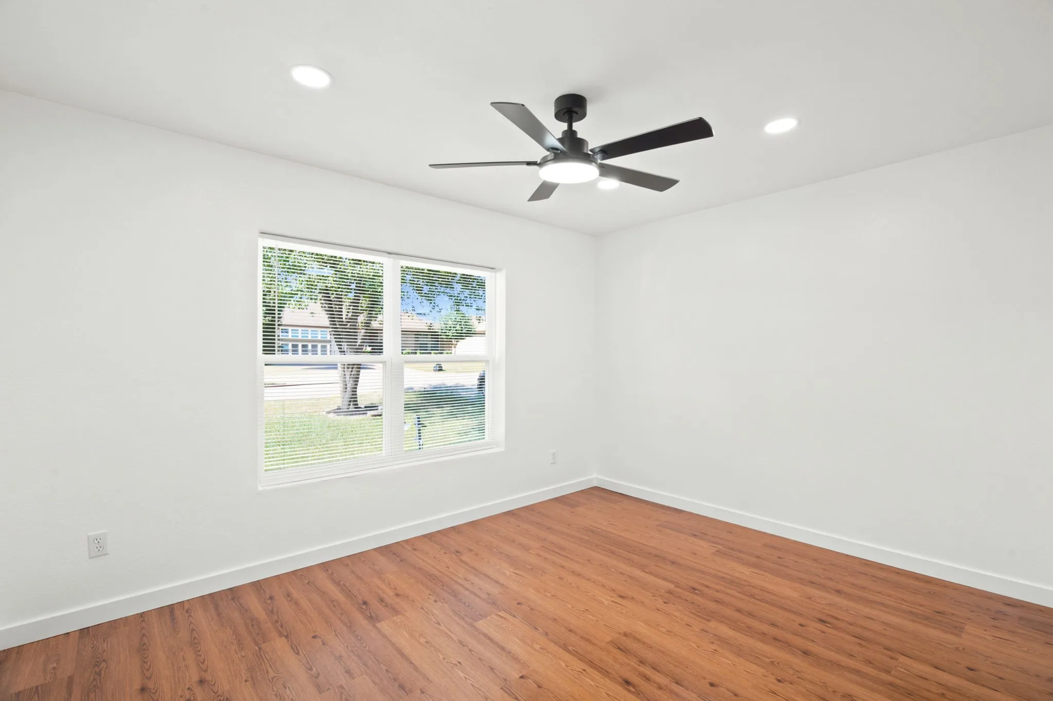Spacious room featuring wood-finish flooring, a modern ceiling fan with integrated lighting, and multiple recessed lights