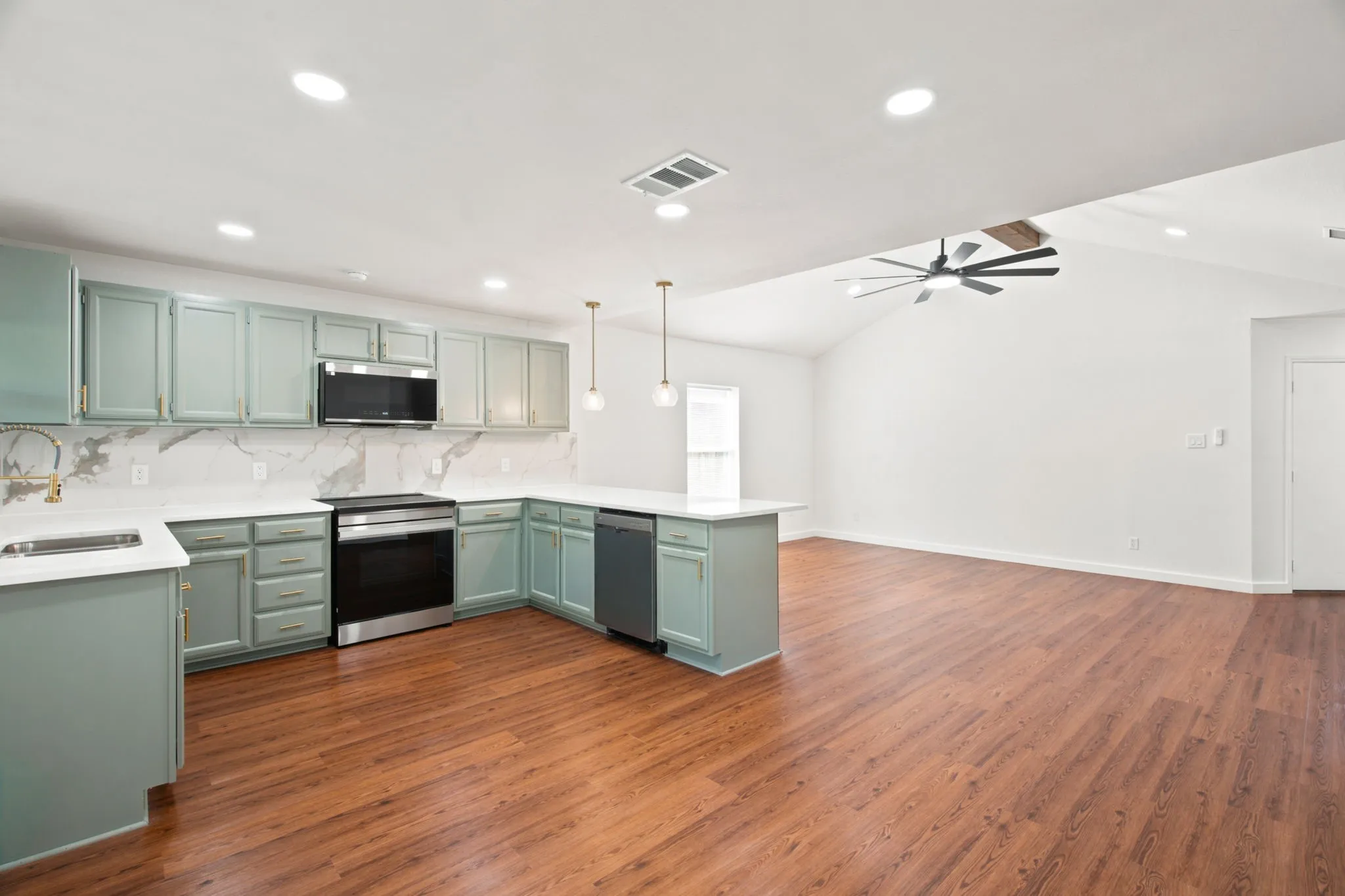 Open-concept kitchen and living area featuring wood-finish flooring, vaulted ceilings, and a contemporary ceiling fan