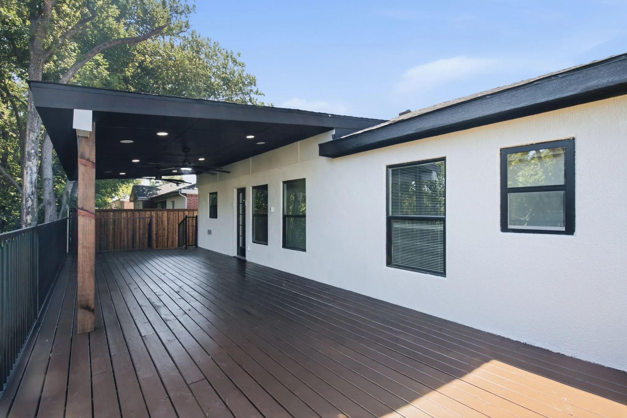 Expansive outdoor deck featuring composite decking, a partial overhead cover with recessed lighting, and a ceiling fan