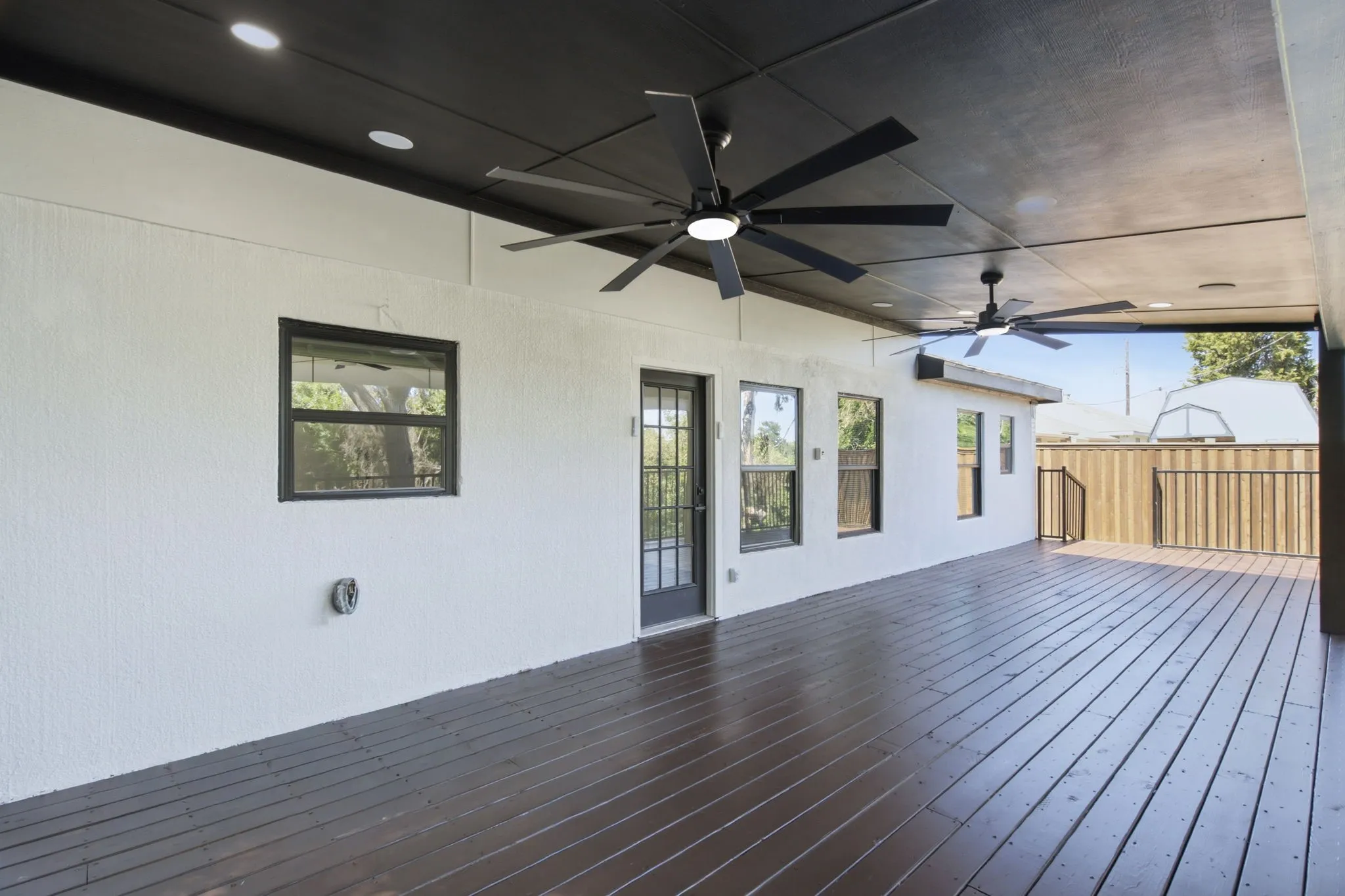 Expansive covered deck featuring dark wood-finish flooring, recessed lighting, and multiple ceiling fans