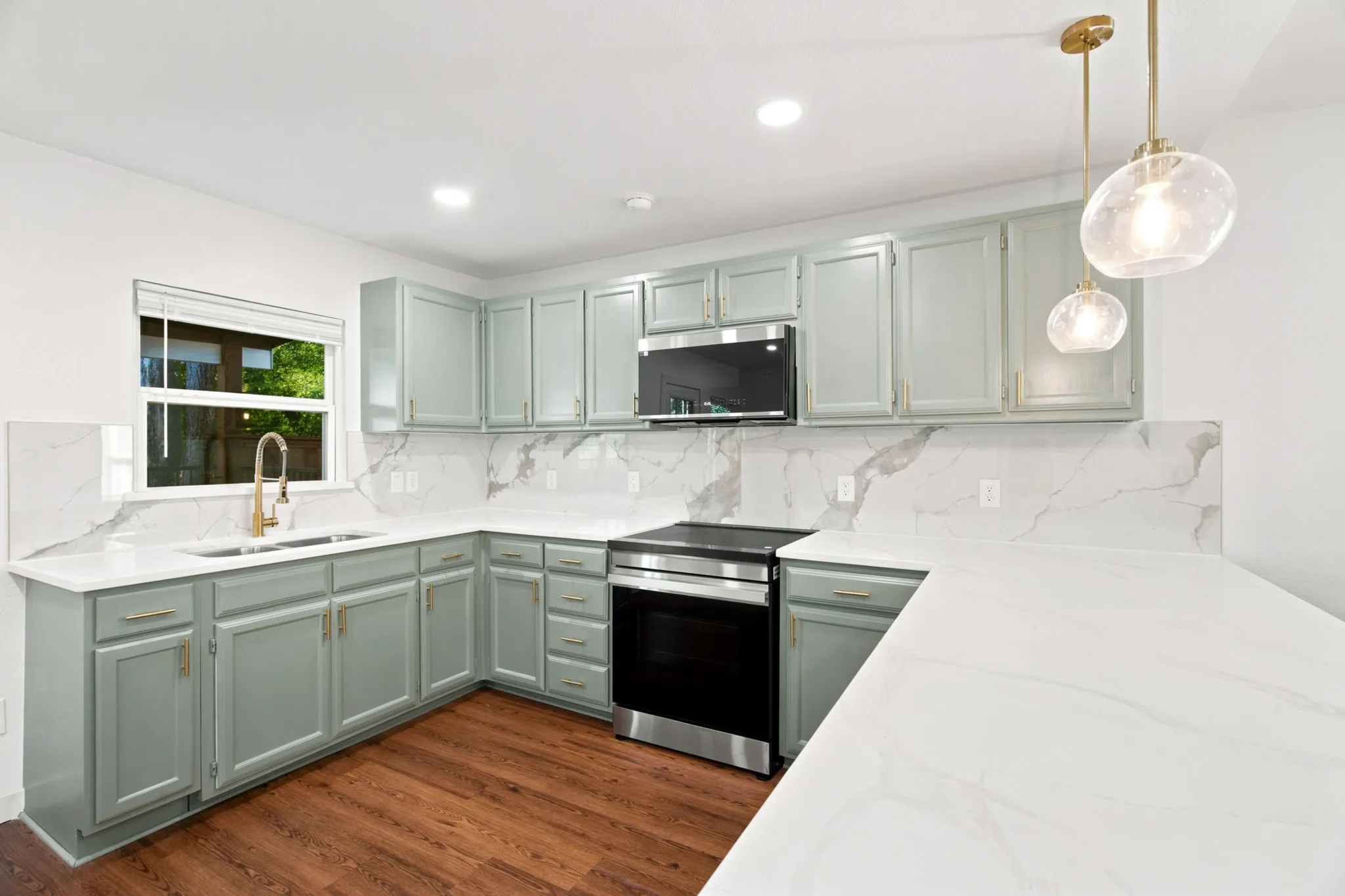 Modern kitchen featuring light green cabinetry, gold hardware, stainless steel appliances, and wood-finish flooring