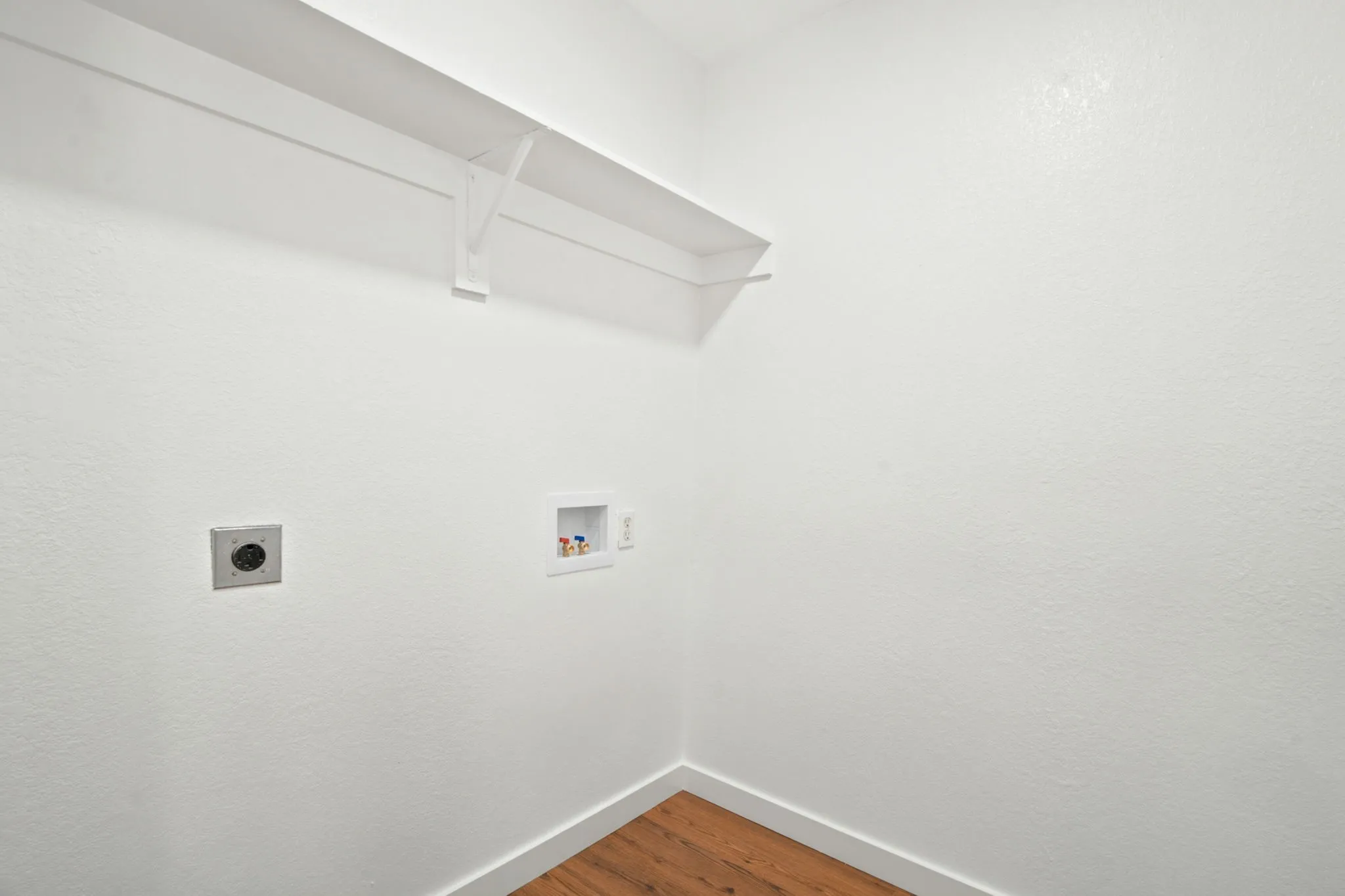 Laundry area featuring a built-in white shelf, white baseboards, and wood-finish flooring