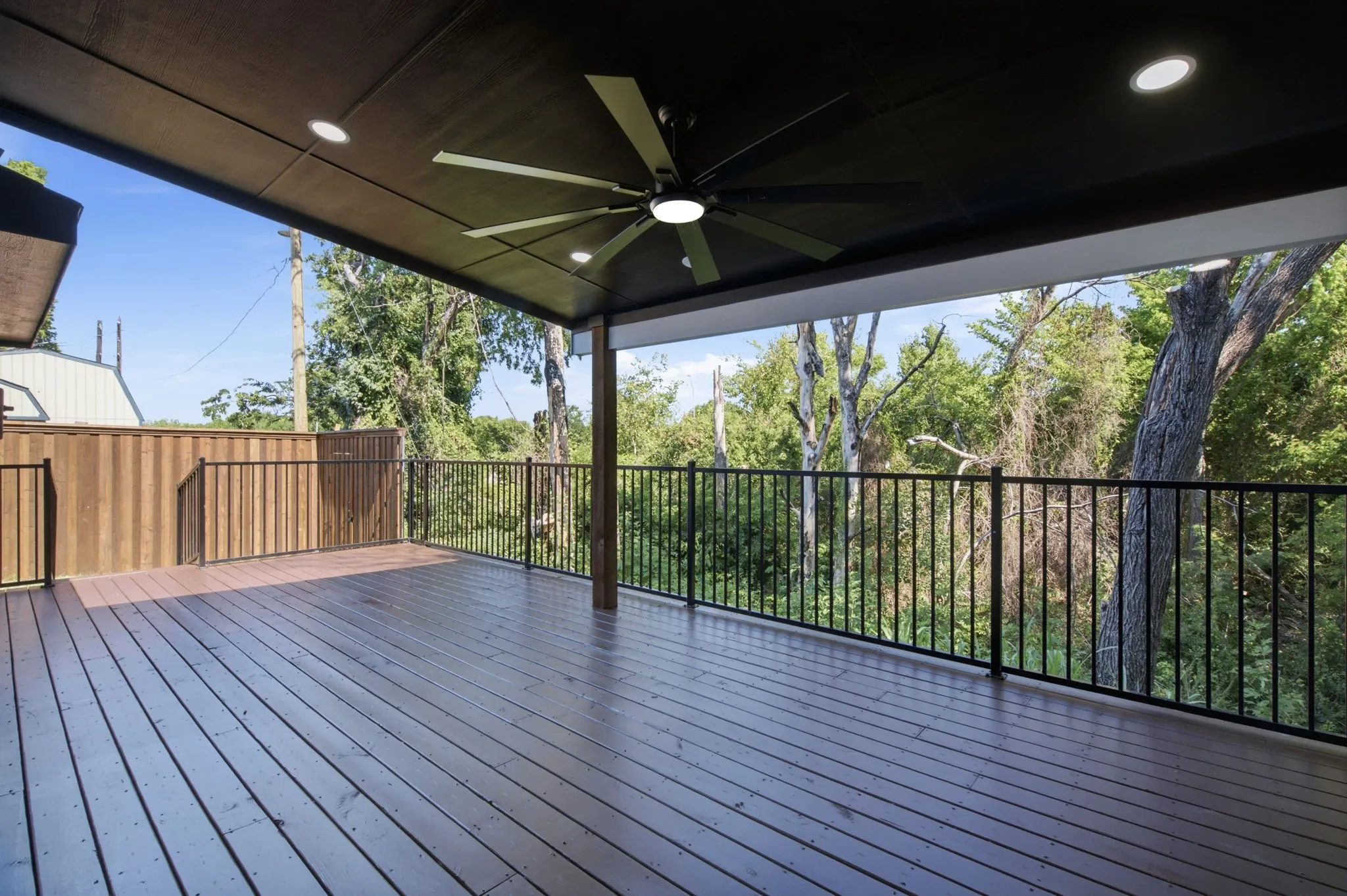 Expansive covered deck featuring wood-finish flooring, black metal railings, and a ceiling fan with integrated lighting