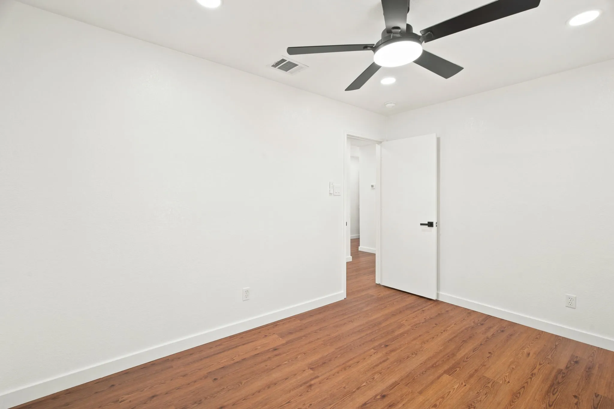 Interior room featuring wood-finish flooring, white walls, and a contemporary ceiling fan with integrated lighting