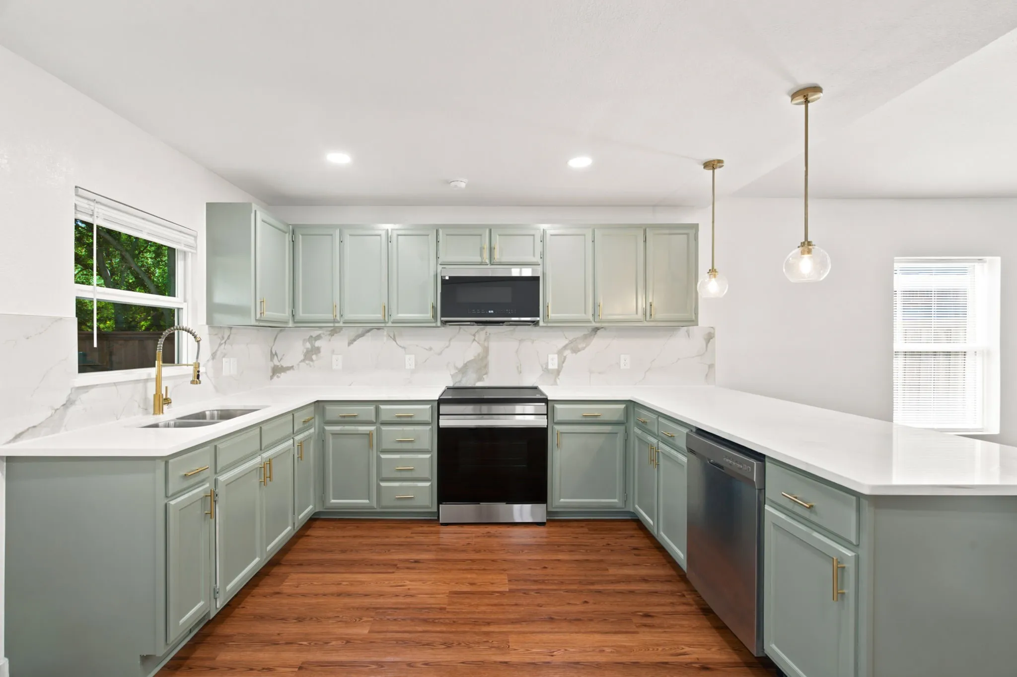 U-shaped kitchen featuring light green cabinetry, white countertops, a white subway tile backsplash with gray veining, stainless steel appliances, and wood-finish flooring