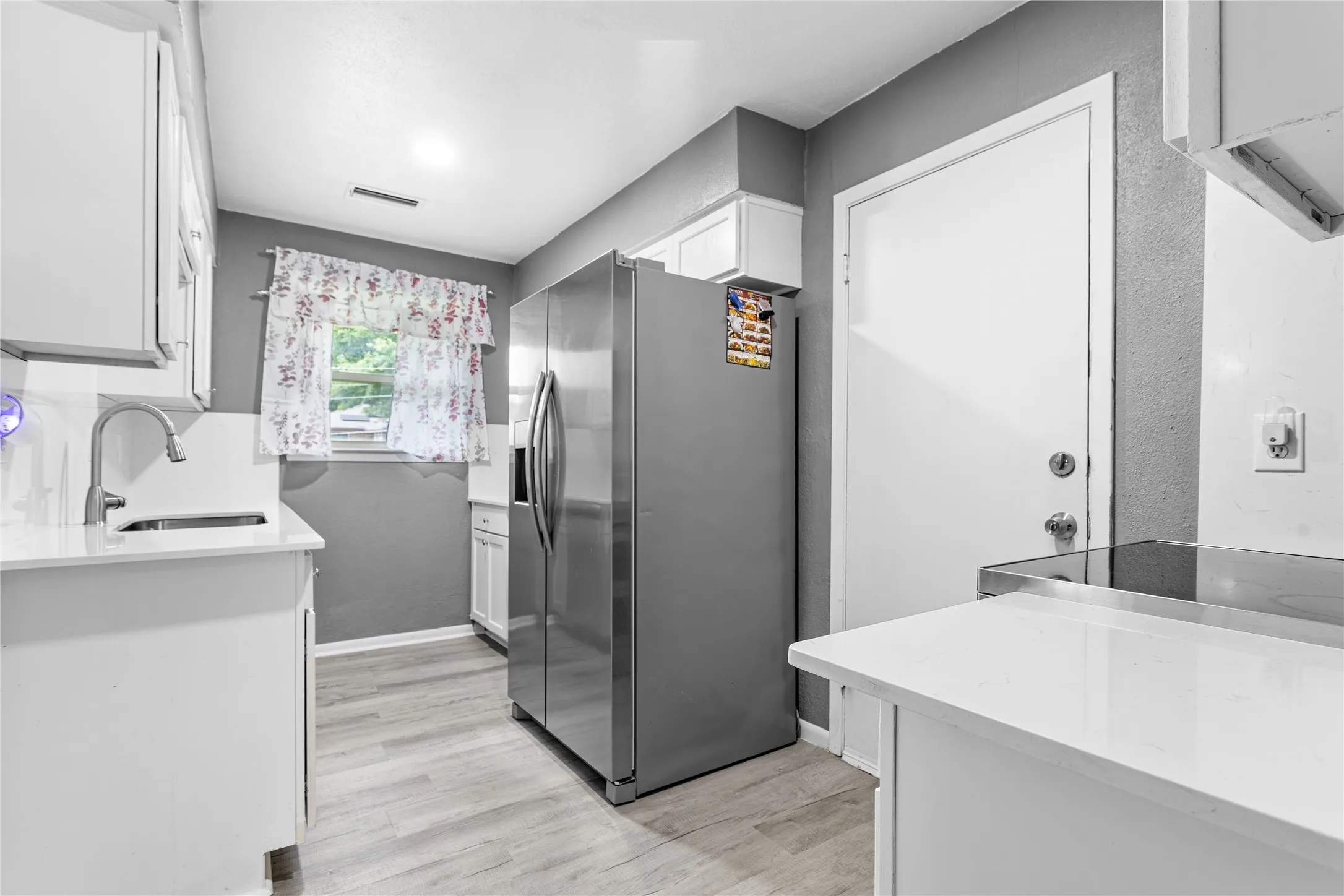 Kitchen featuring a stainless steel refrigerator, white cabinetry, light-toned countertops, wood-finish flooring, and a window