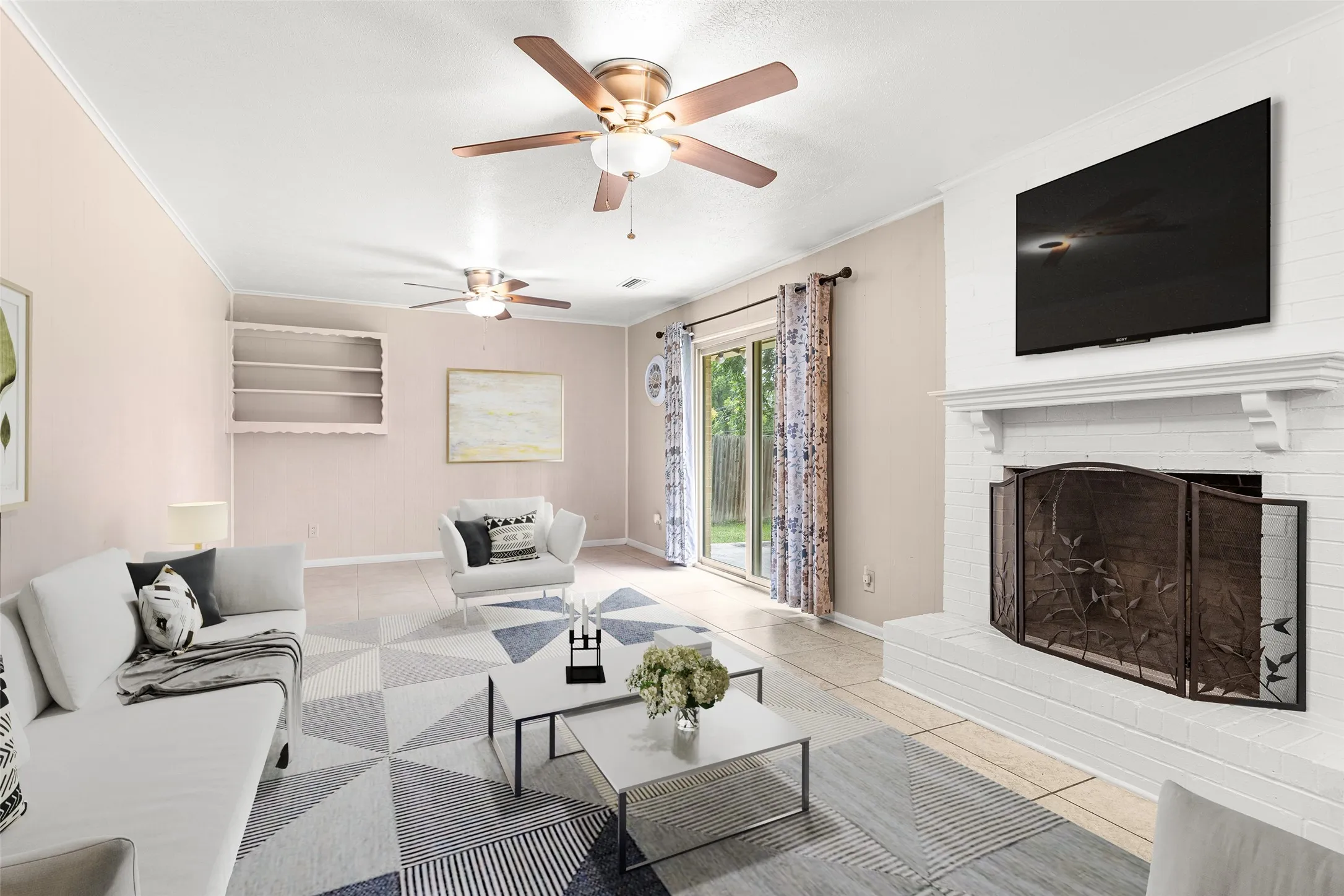 Virtually Staged Spacious living area featuring a brick fireplace with a decorative mantel, ceiling fans, built-in shelving, and sliding glass doors leading to the exterior