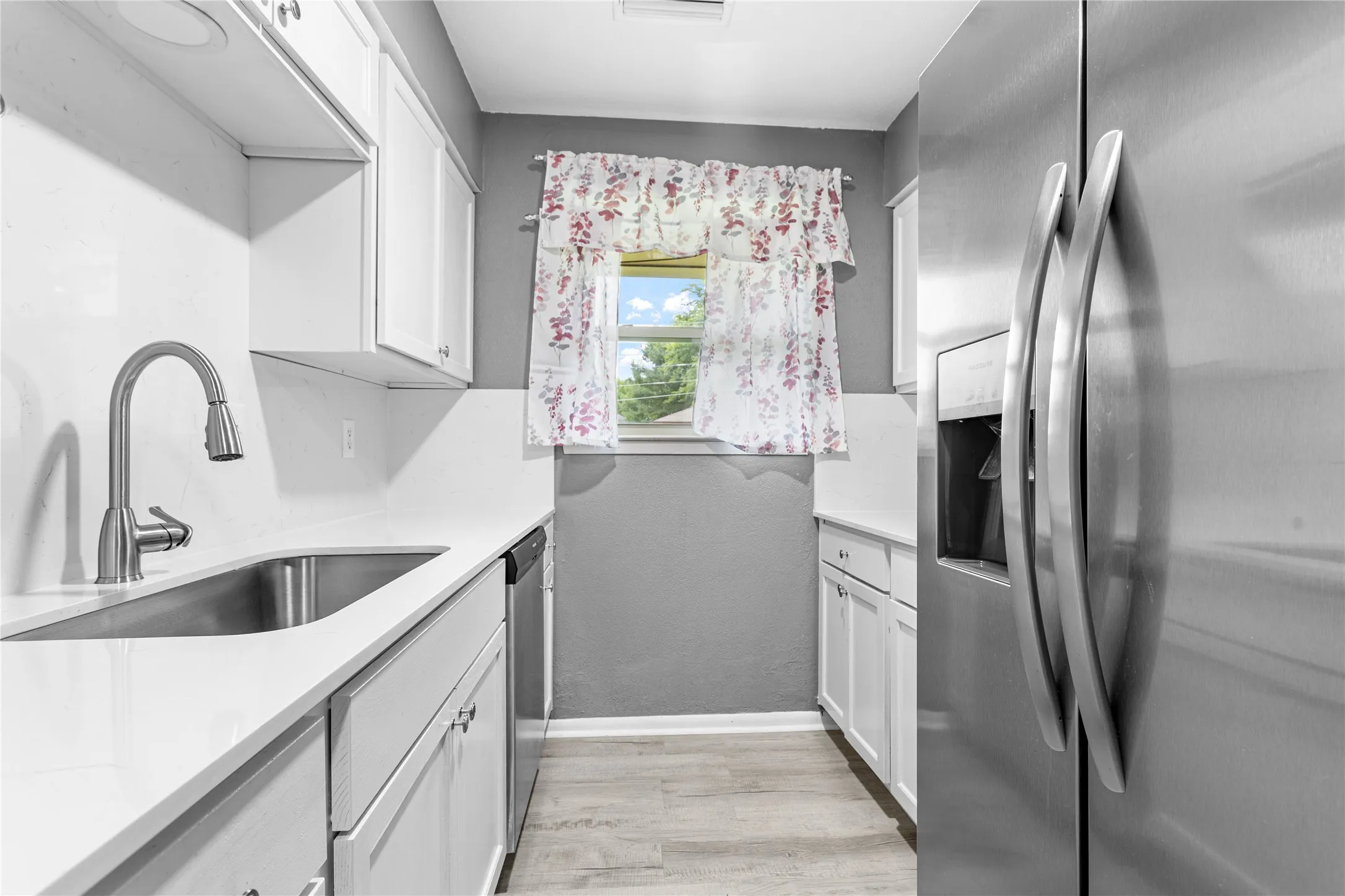 Kitchen featuring white cabinetry, light-toned countertops, a stainless steel sink with a gooseneck faucet, a stainless steel refrigerator, and wood-finish flooring