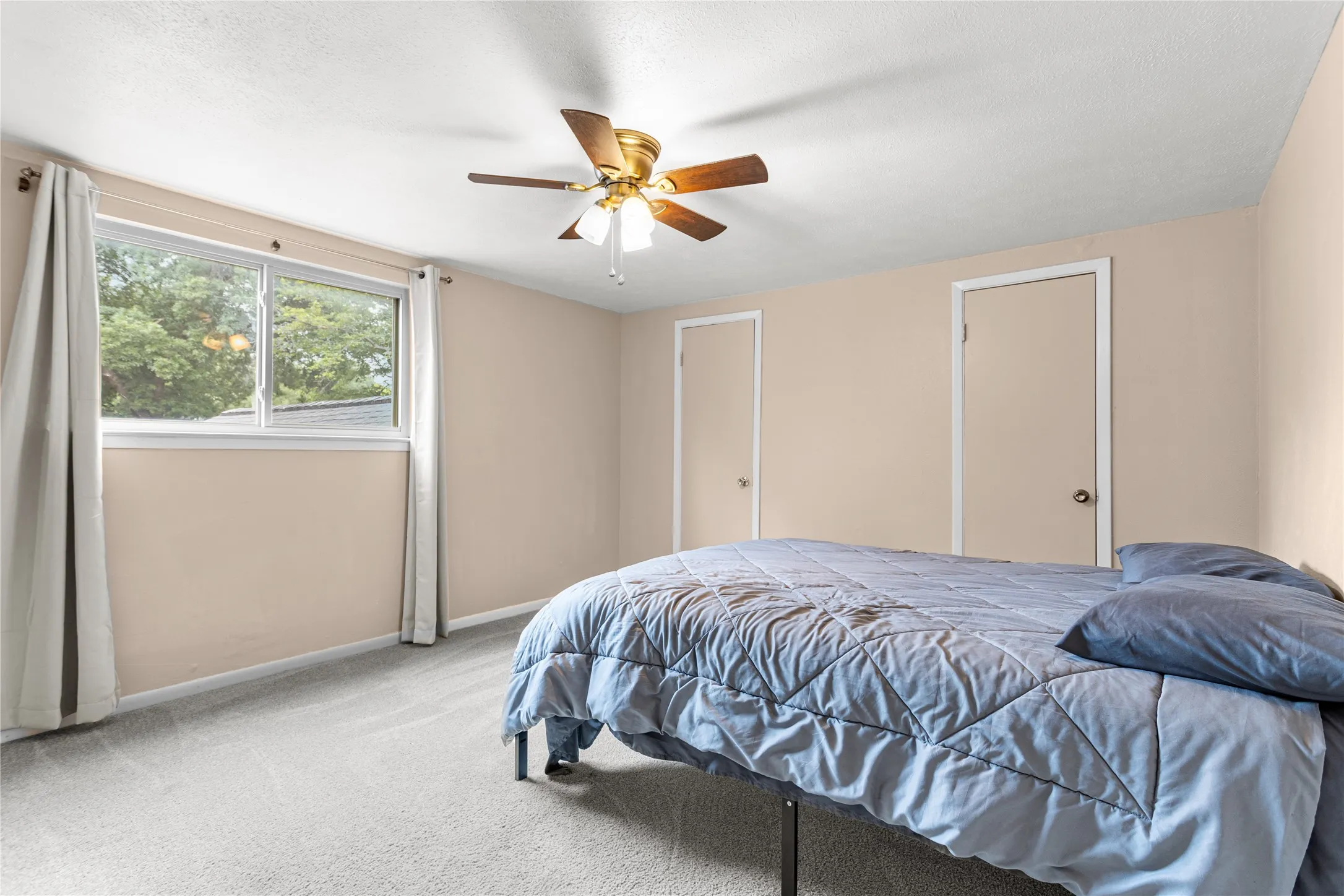 Spacious room featuring light-colored walls, soft carpeting, and a ceiling fan with integrated lighting