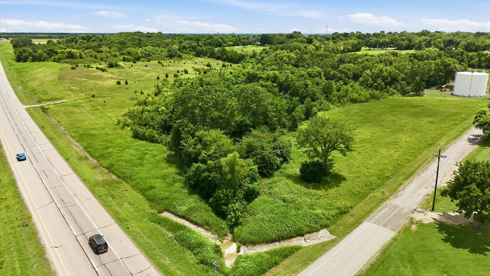 Expansive green parcel featuring extensive tree coverage, a prominent roadway frontage, and an adjacent service road