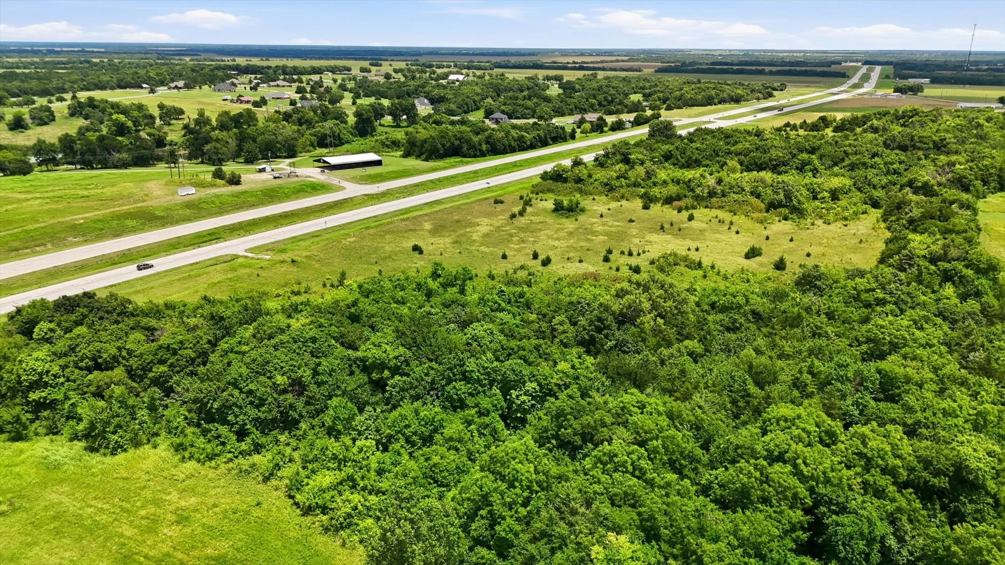 Expansive land featuring significant tree coverage, open grassy areas, and highway frontage