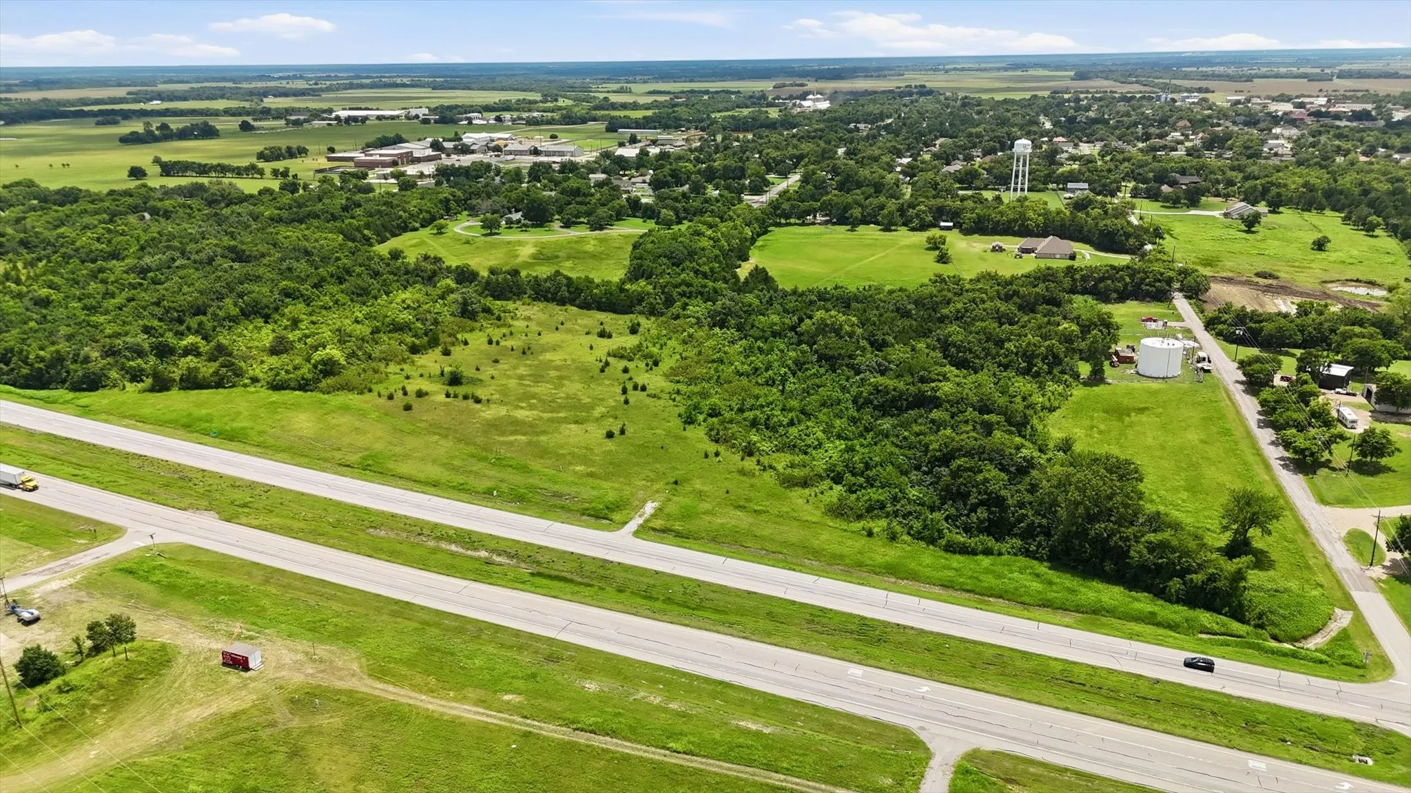 Expansive green acreage with a prominent roadway and scattered wooded areas