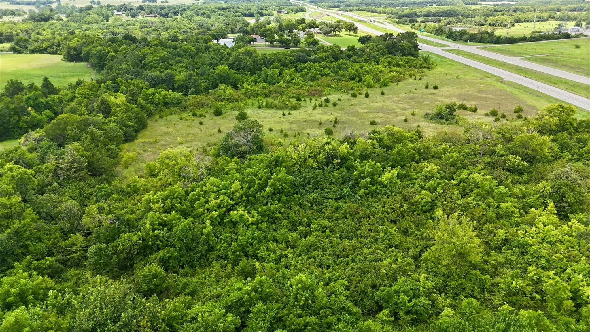 Expansive acreage featuring mature trees and open grassy areas, bordered by a multi-lane roadway