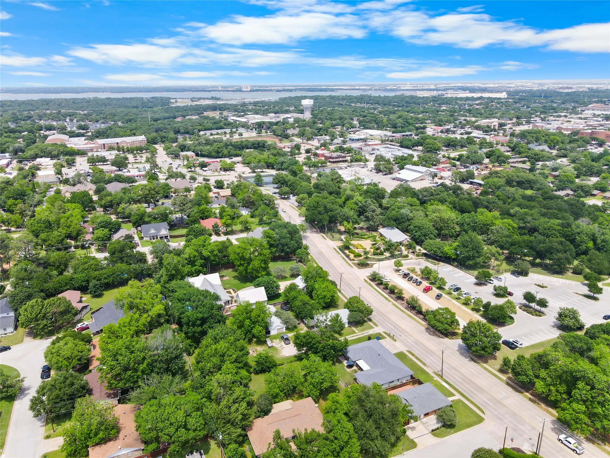 Expansive aerial perspective showcasing a residential area with mature tree coverage, a prominent roadway, and commercial parking areas