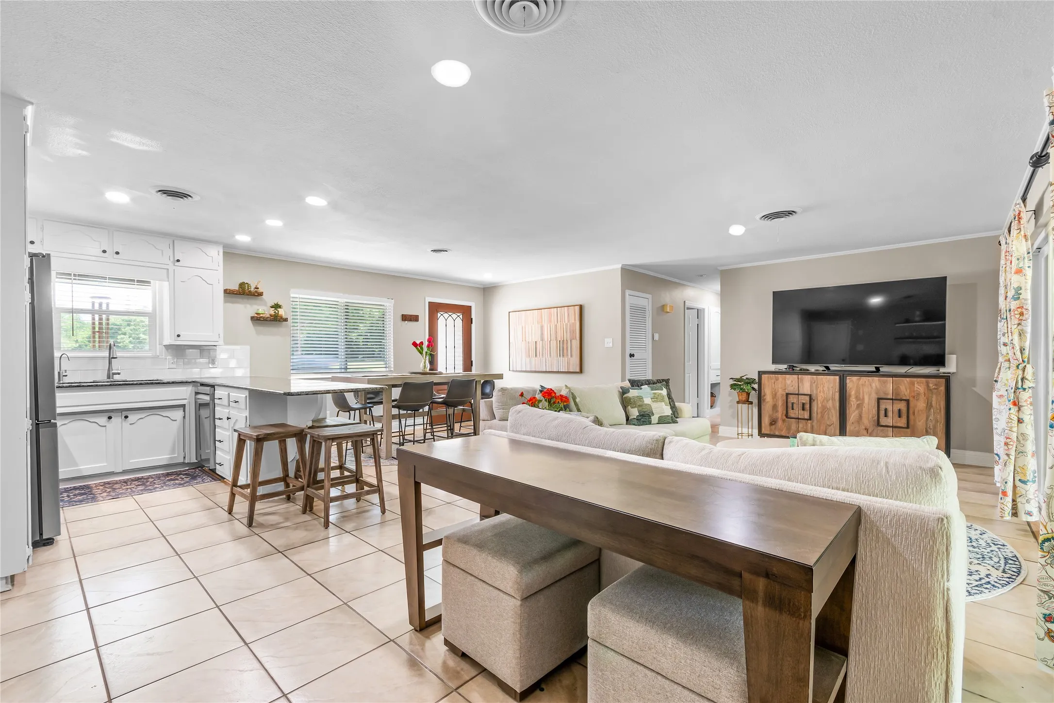 Open-concept living area featuring a kitchen with white cabinetry, a stainless steel refrigerator, and a light-toned countertop