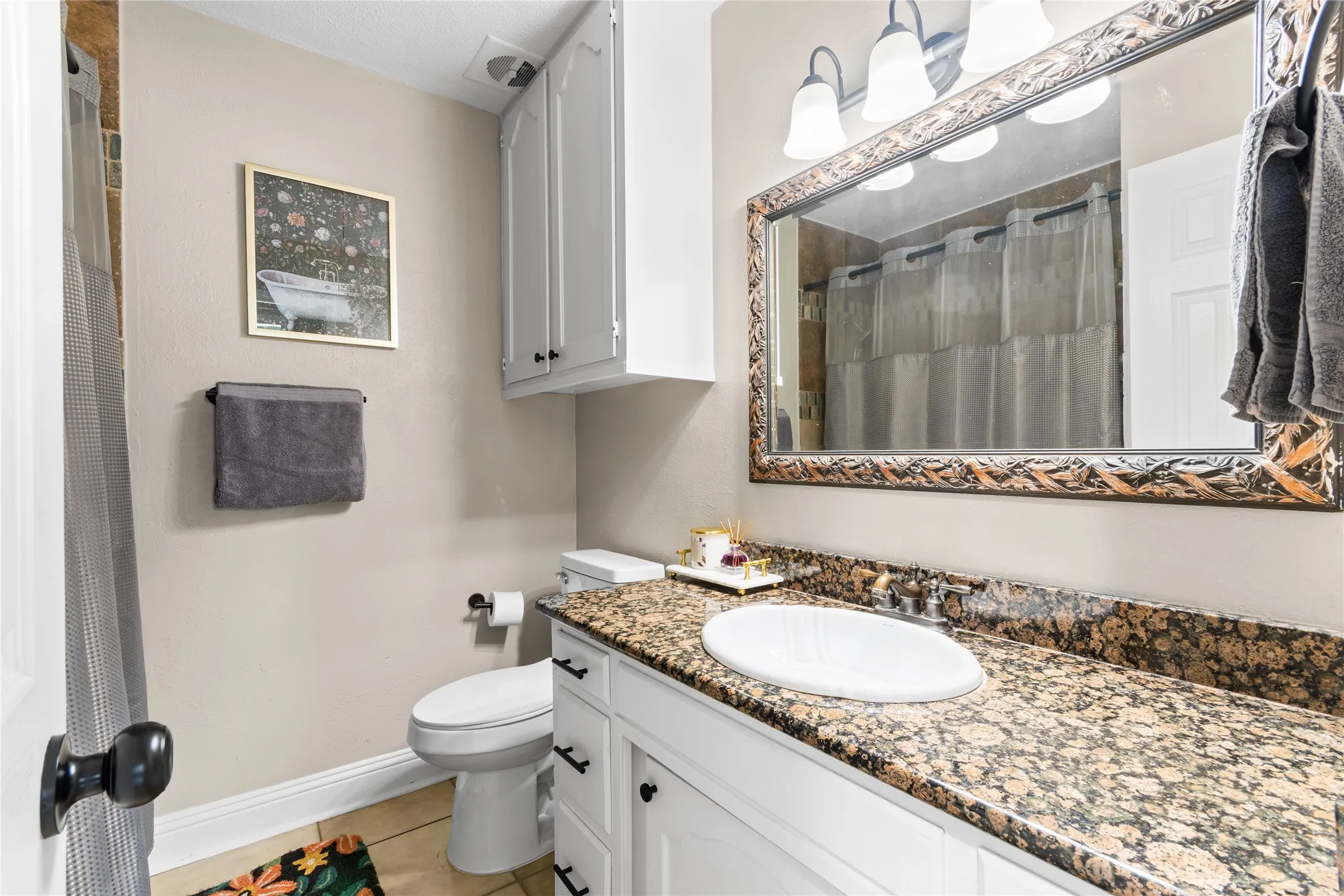 Bathroom featuring a single vanity with granite countertop and undermount sink, white cabinetry with black hardware, and a framed mirror with integrated lighting