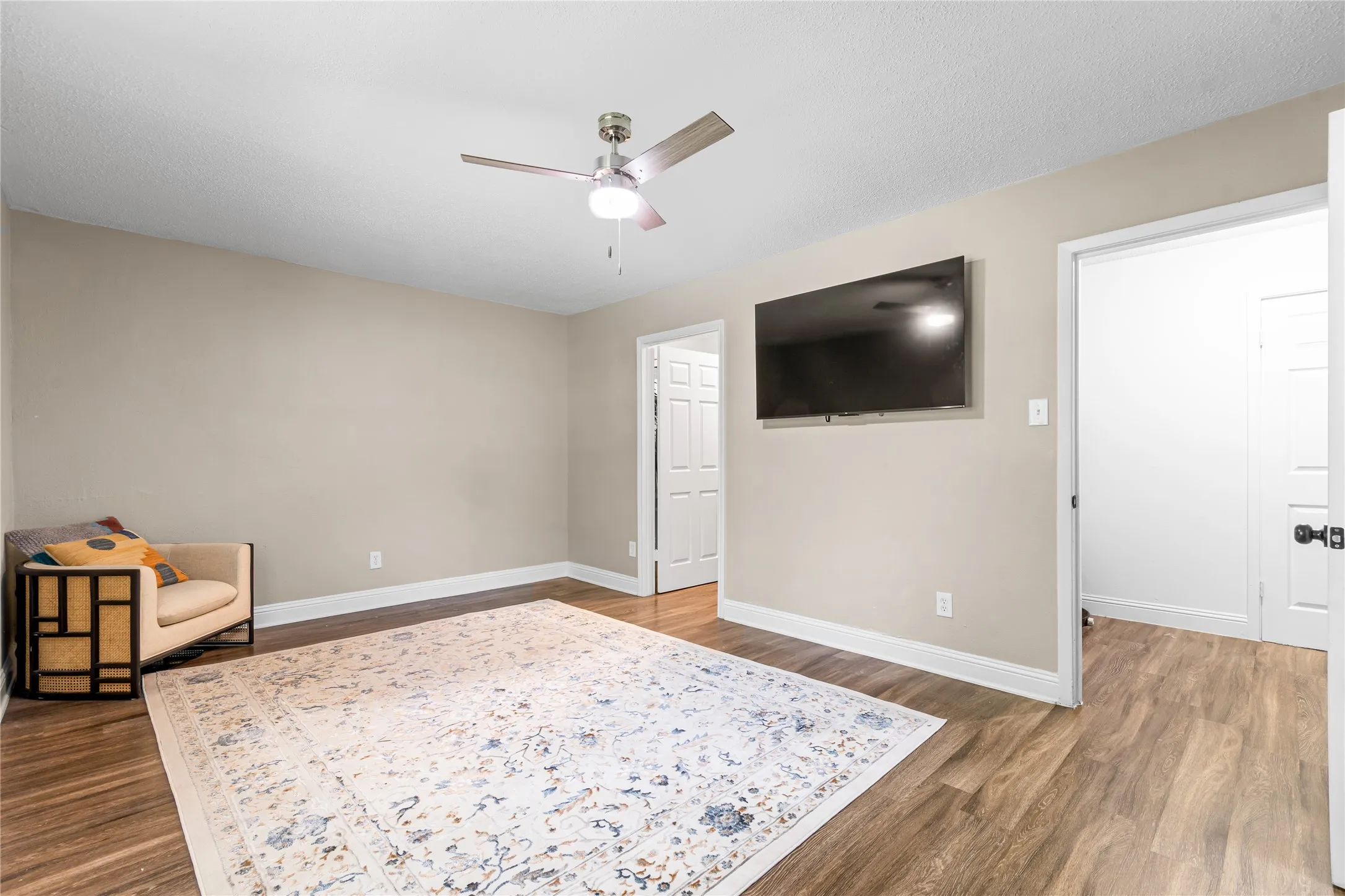 Spacious room featuring woodlike-finish flooring, neutral paint tones, a ceiling fan with integrated lighting, and multiple interior doorways. Step out onto a covered patio to enjoy your cup of coffee
