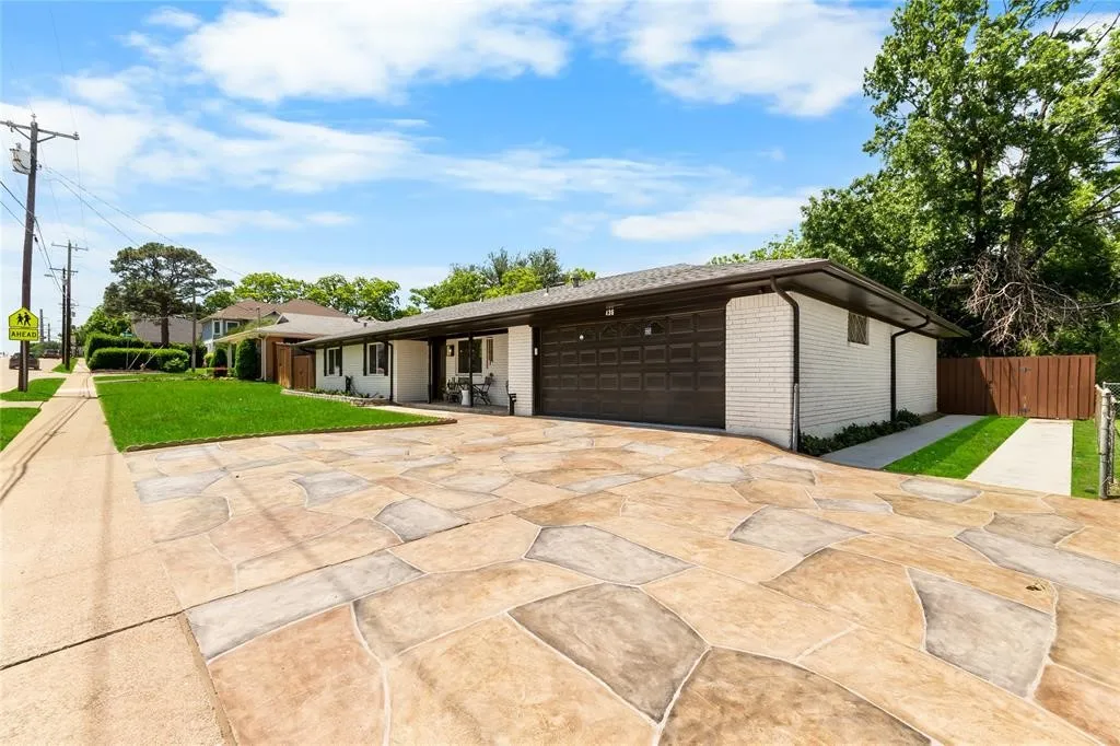 White brick exterior with a dark brown garage door, patterned stone-look driveway, and a manicured lawn