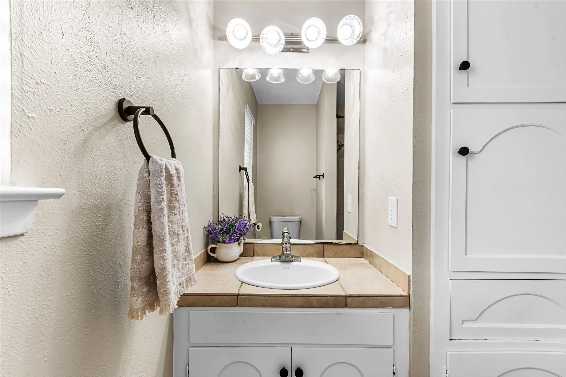 Casita Bathroom featuring a single basin vanity with tile countertop, white cabinetry with black hardware, and a framed wall mirror