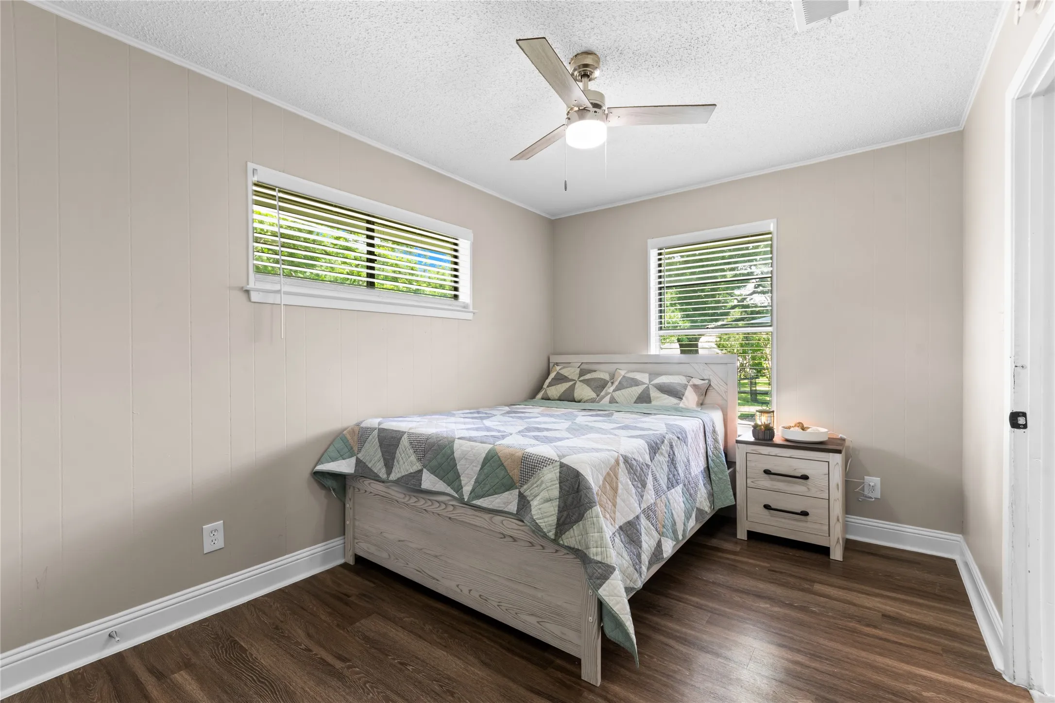 Casita Spacious room featuring wood-finish flooring, two windows with blinds, a ceiling fan with integrated lighting, and neutral wall paneling