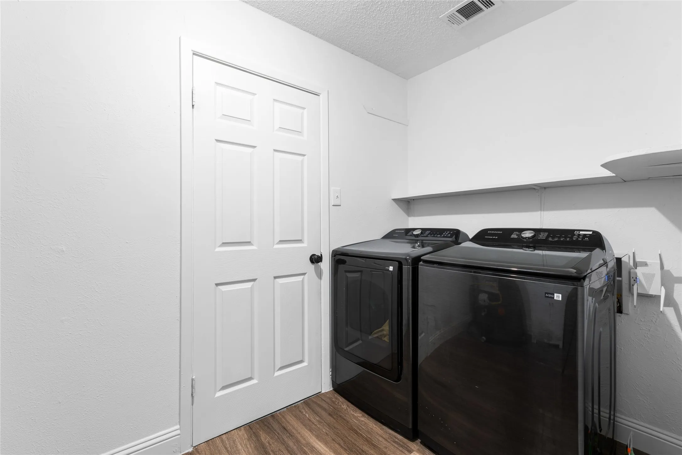 Dedicated laundry area featuring wood-finish flooring and a white wall shelf