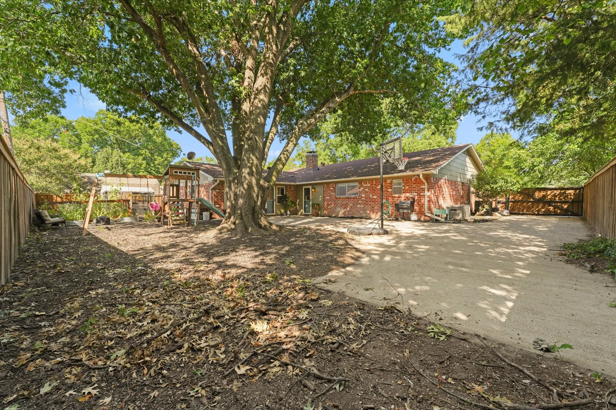 Oversized backyard shaded by mature trees with an expansive concrete patio, plenty of room for entertaining, play, gardening, or future outdoor living, plus a storage building and privacy fence.