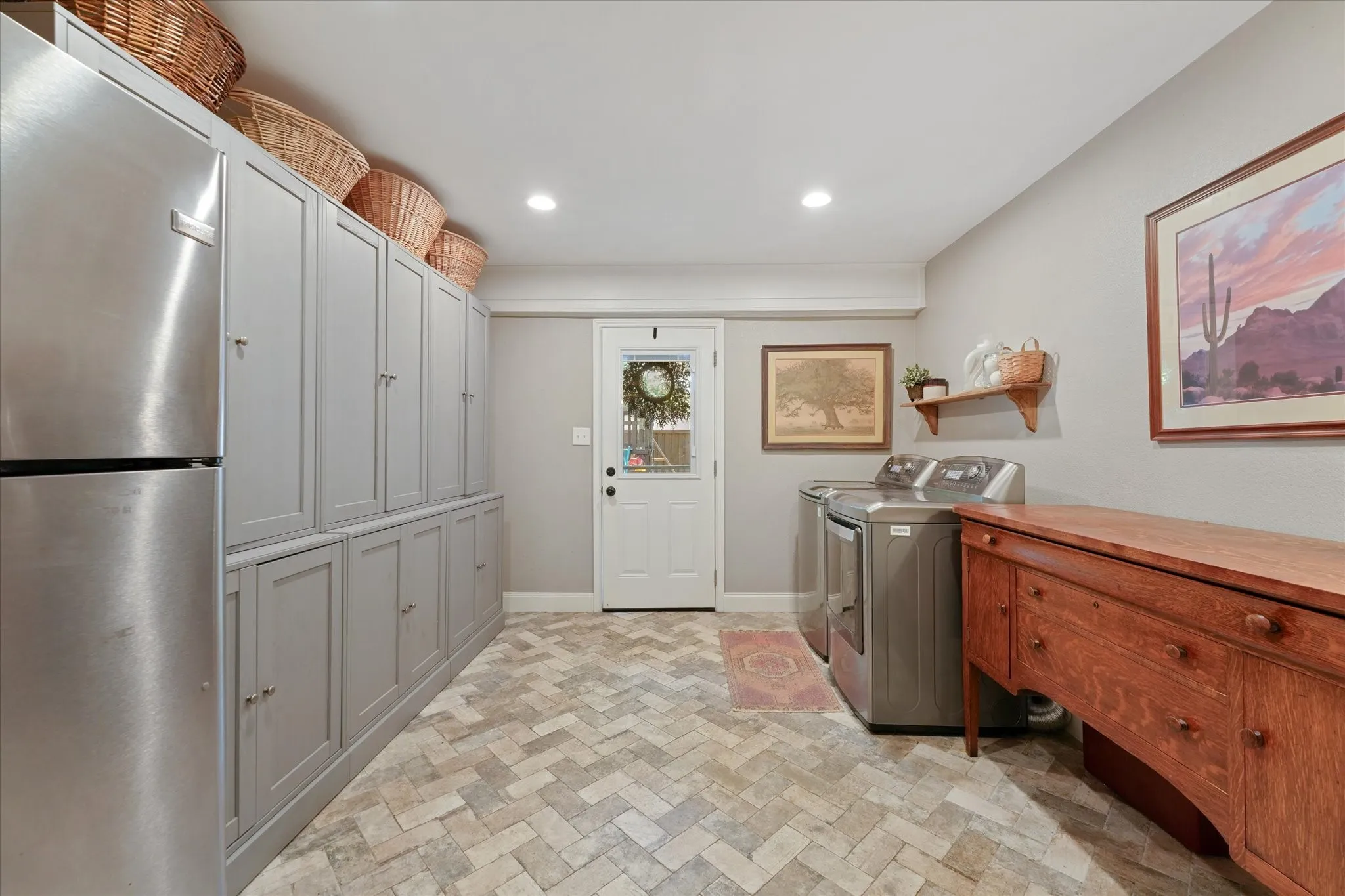 Spacious utility room with abundant custom storage cabinets, room for a second refrigerator, full-size washer and dryer area, and direct access to the backyard.