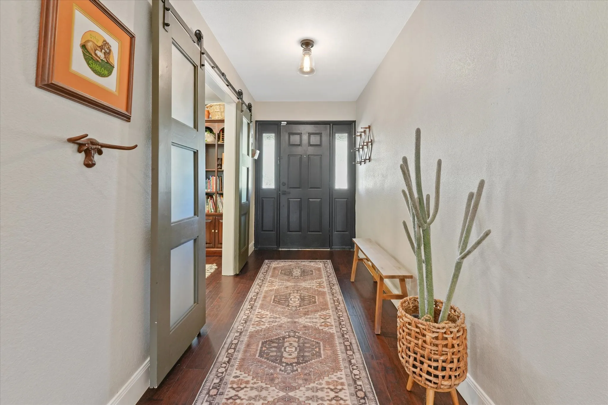 Long welcoming foyer with hardwood floors, updated front door, and sliding barn doors opening to a private flex room or home office.