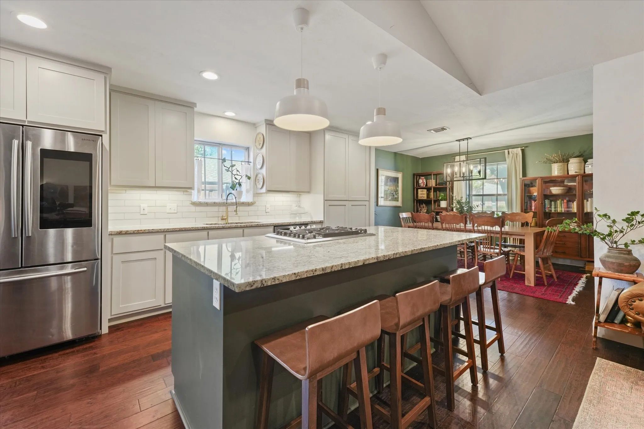 Expansive kitchen with a large island offering seating for four, granite countertops, gas cooktop, updated lighting, and open access to the dining room.