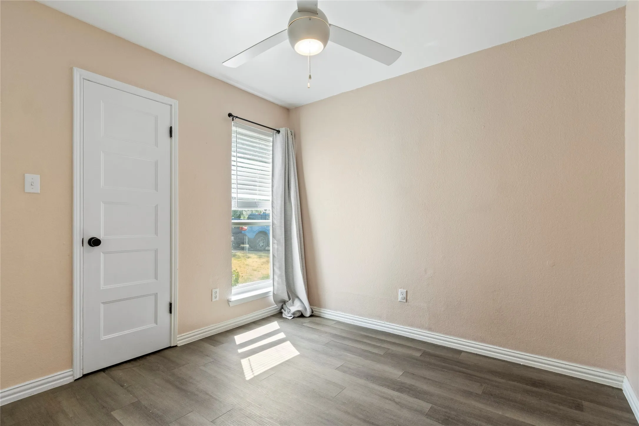 Wood-finish flooring, light neutral-toned walls, and a white ceiling fan with integrated lighting